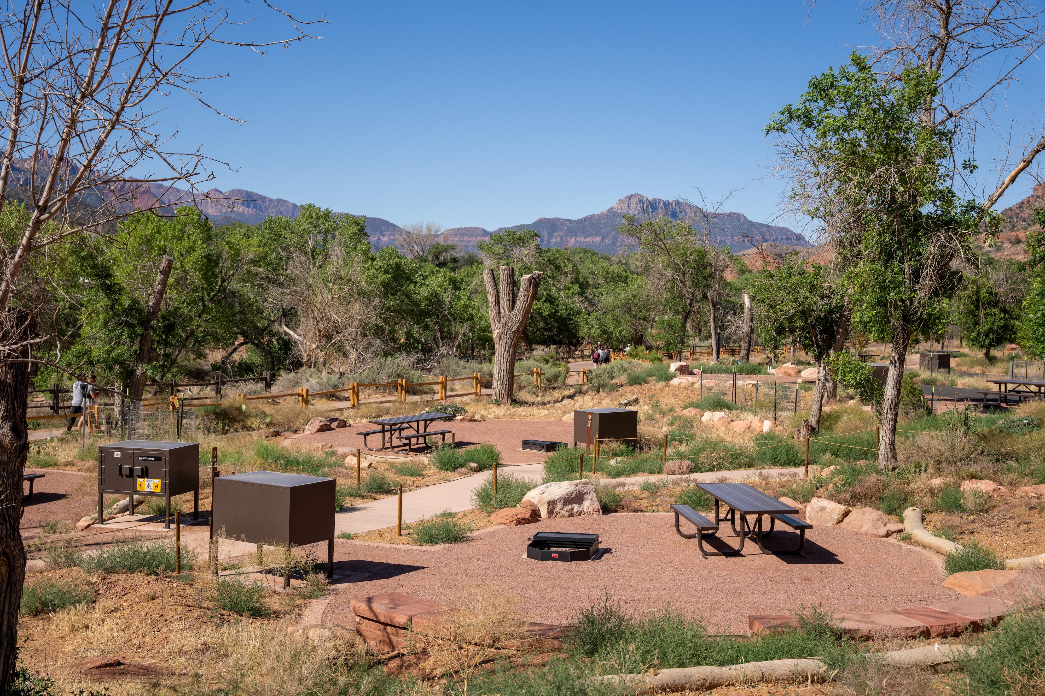 A grassy campground with flat, gravel sites and a nearby paved pathway.