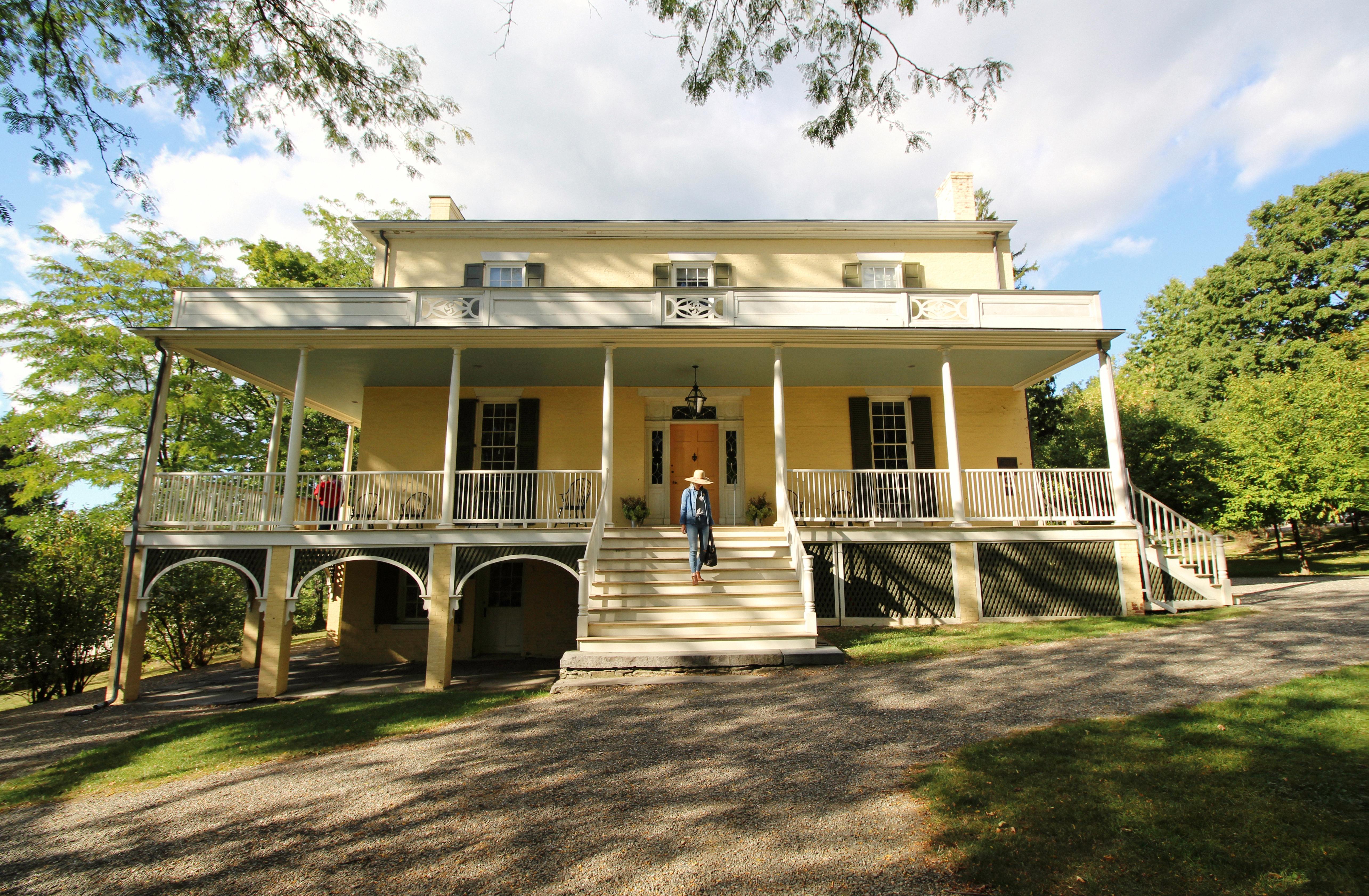 A three story house with large porch across the front and flight of steps leading to the ground.