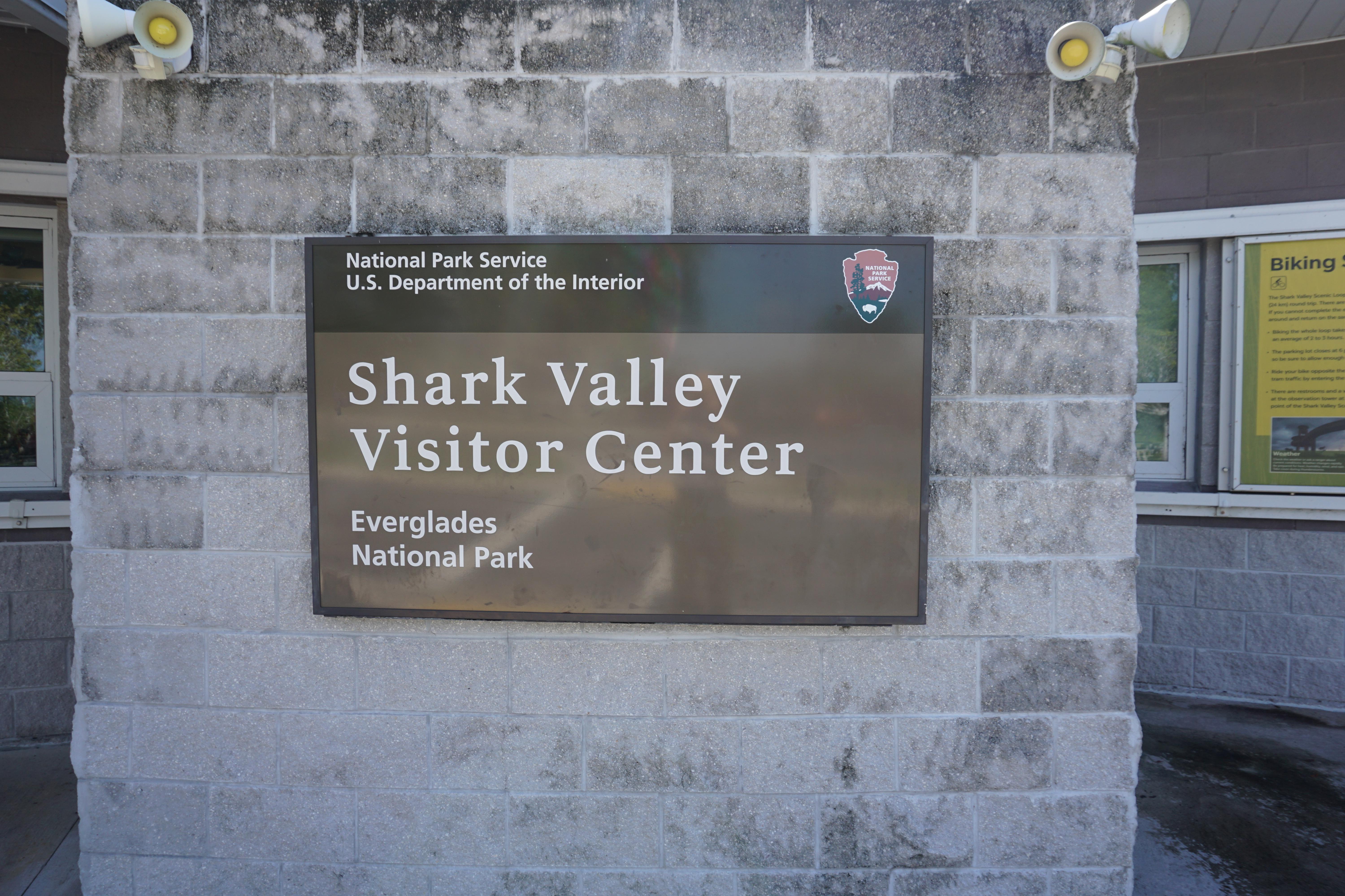A sign reading 'Shark Valley Visitor Center' hangs on a concrete wall