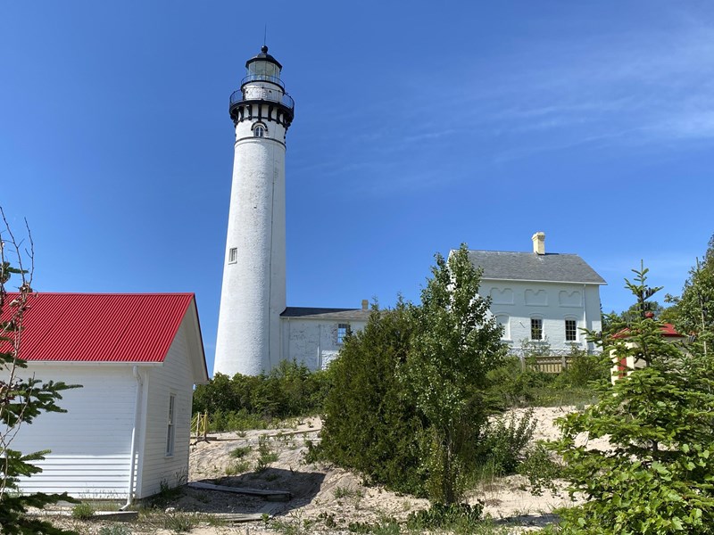 A white lighthouse next to a two story brick building with a red roofed building in the foreground.