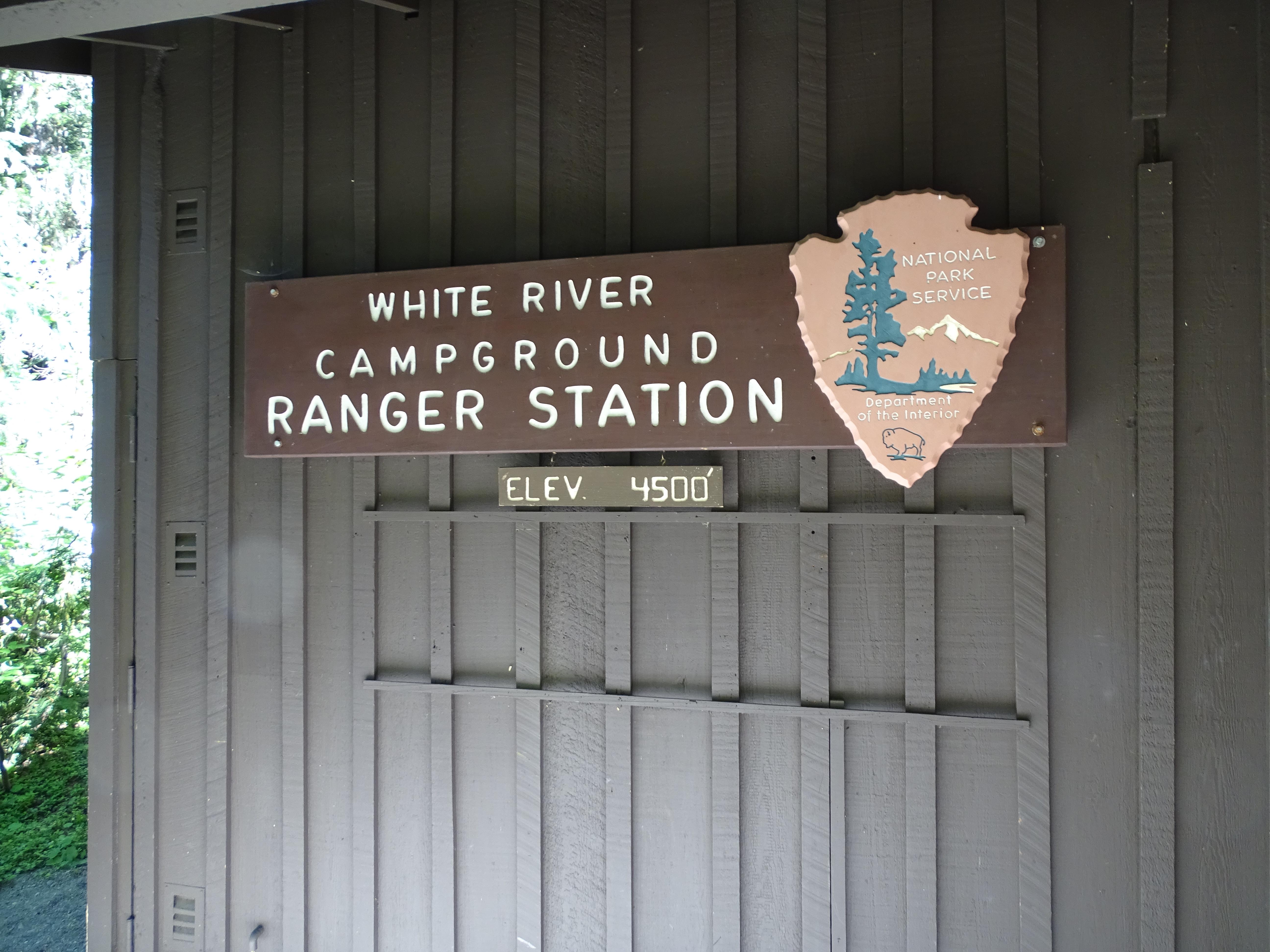 A brown wall with a sign for the ranger station with a large park service arrow head.