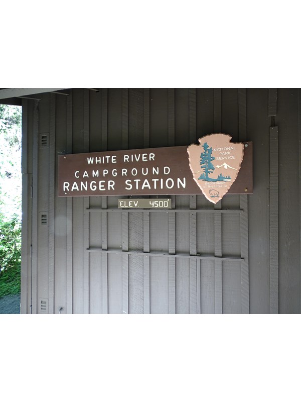 A brown wall with a sign for the ranger station with a large park service arrow head.