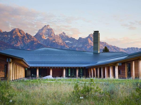 Teton Range rises behind a building with a log supported angular roof surrounding a courtyard