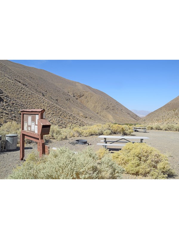 Eye level bulletin board stands on 2 wood posts. Wood box with hinged top opening attached to side.