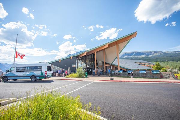 The pointed roof of the St. Mary Visitor center juts into the sky on a sunny summer day. People stan