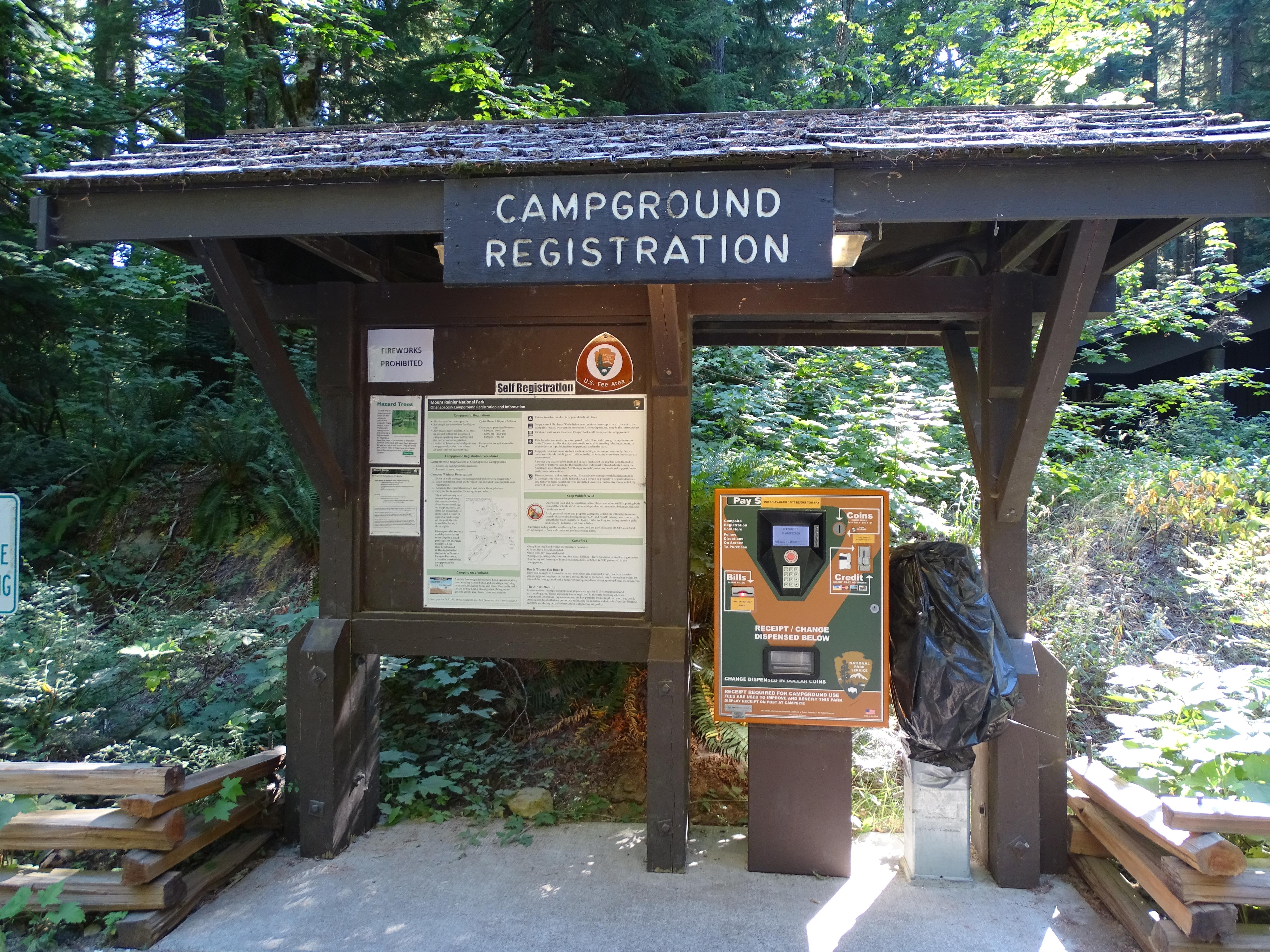 A brown bulletin board with information about the campground and a machine for paying the fee.