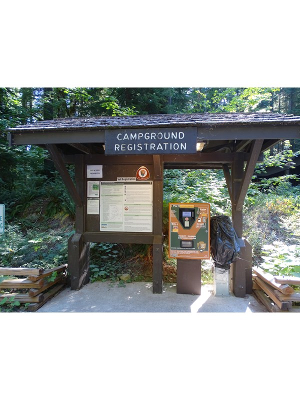 A brown bulletin board with information about the campground and a machine for paying the fee.