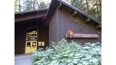 A large brown building with a slanted roof surrounded by forest.