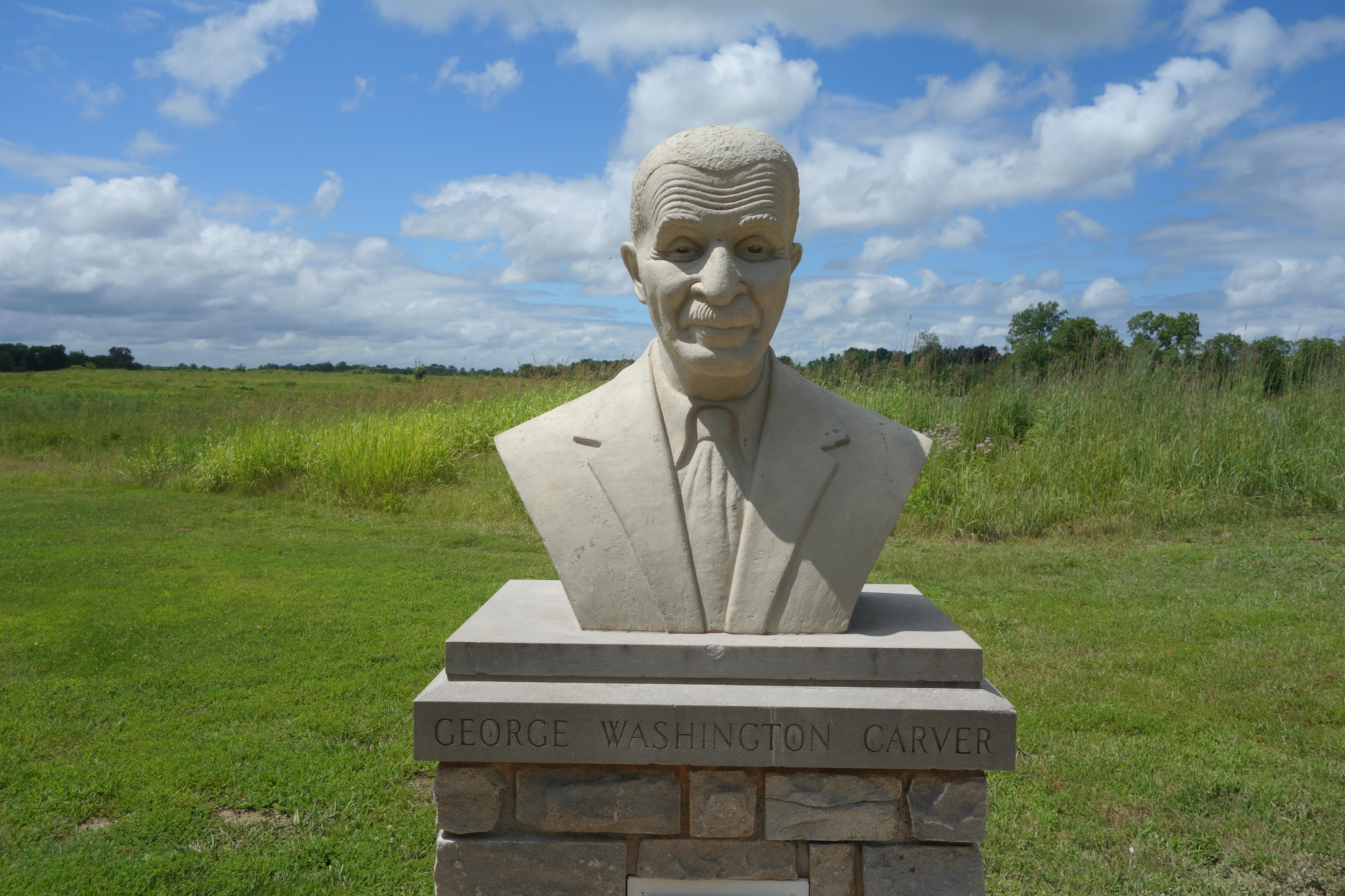 A cast concrete bust of George Washington Carver and prairie in the background.