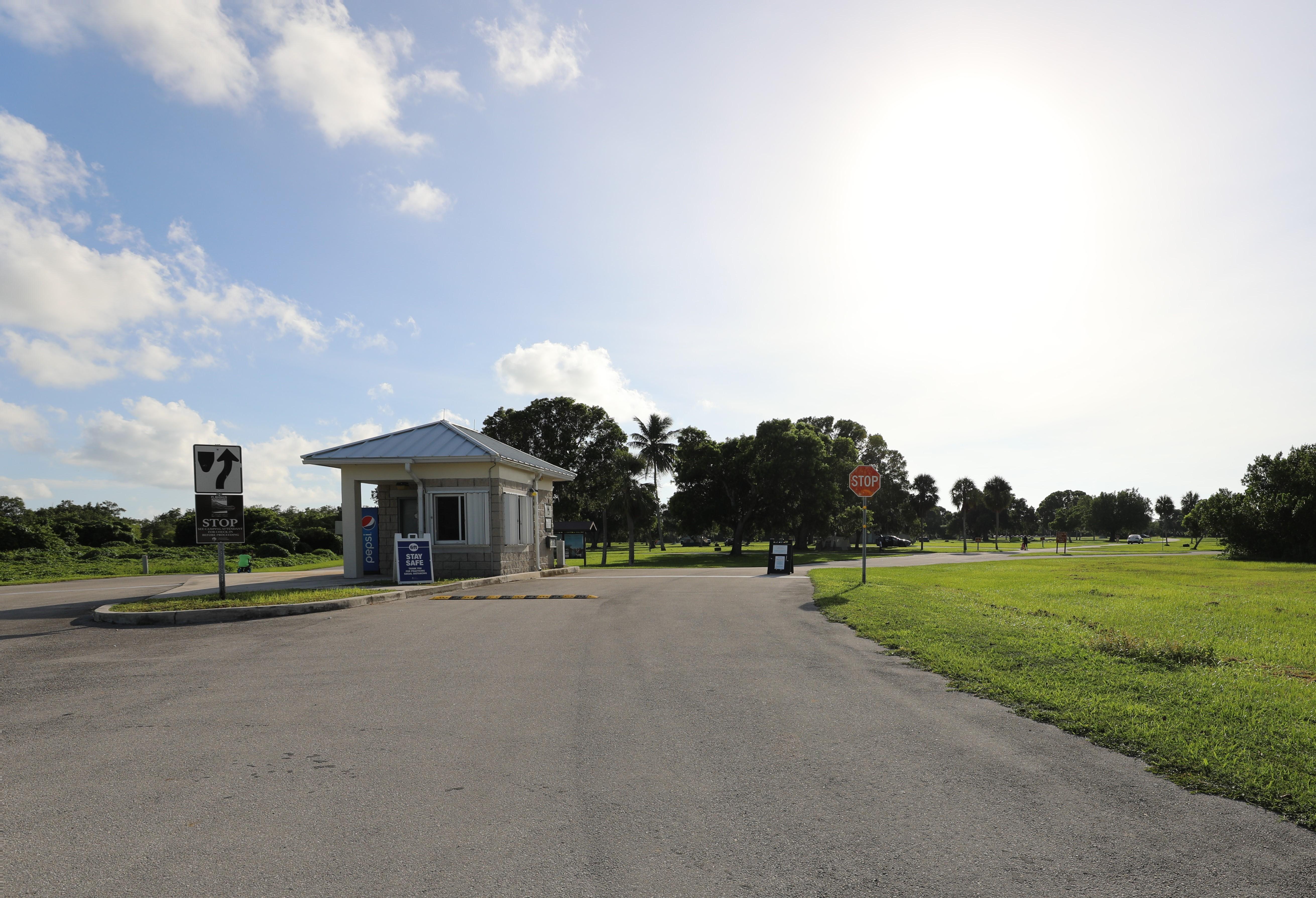 A white entrance building stands alongside a road with green grass and trees in the distance