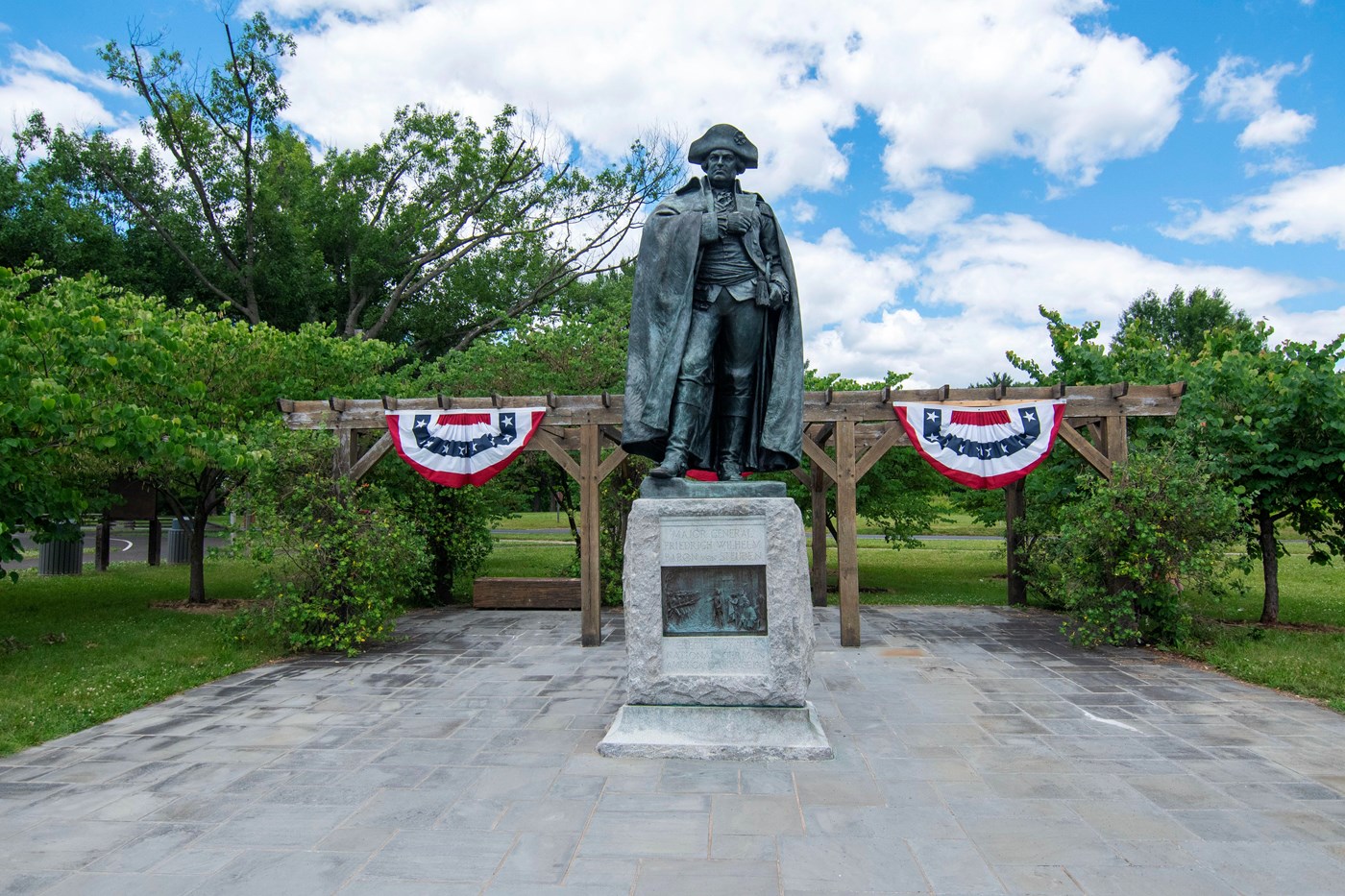 bronze statue of rev war general on stone base, red white and blue bunting behind