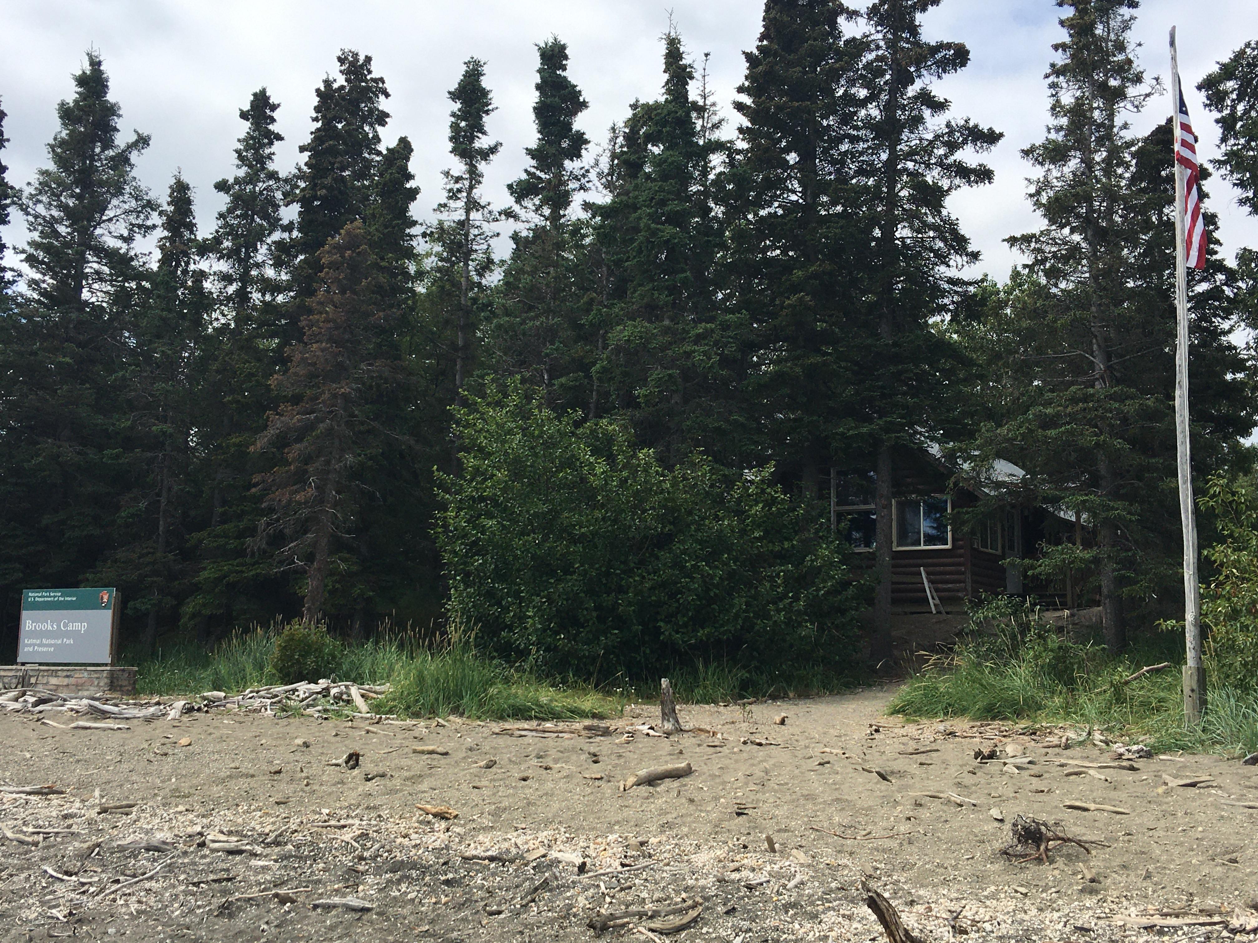 Brooks Camp sign, visitor center, trail, and flag pole as seen from the beach when a visitor arrives