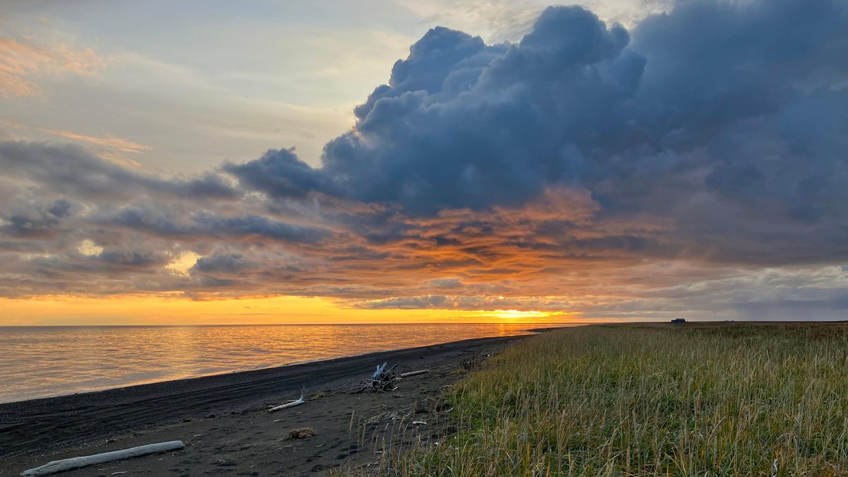 Orange and red sky as the sun sets along the Cape Krusenstern coast. Sun set reflects on the water. 