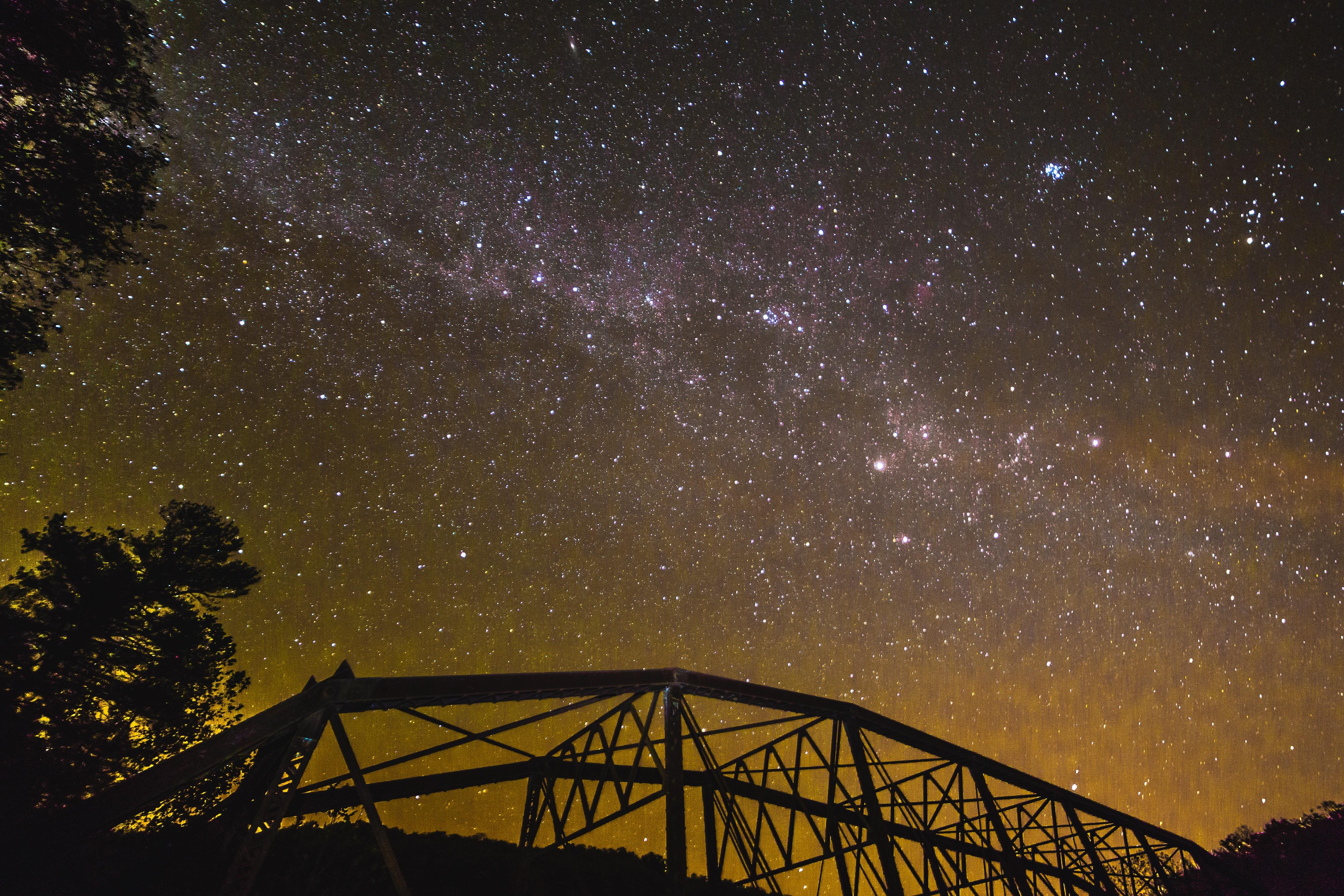 A star-filled night sky above the silhouette of a truss-bridge