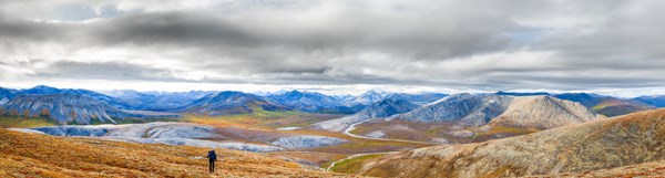 Hiker on the tundra. Snow covered mountains and a river in the dramatic background.