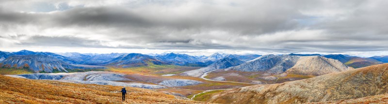 Hiker along the Nakolik drainage Hiker on the tundra. Snow covered mountains and a river in the dramatic background.