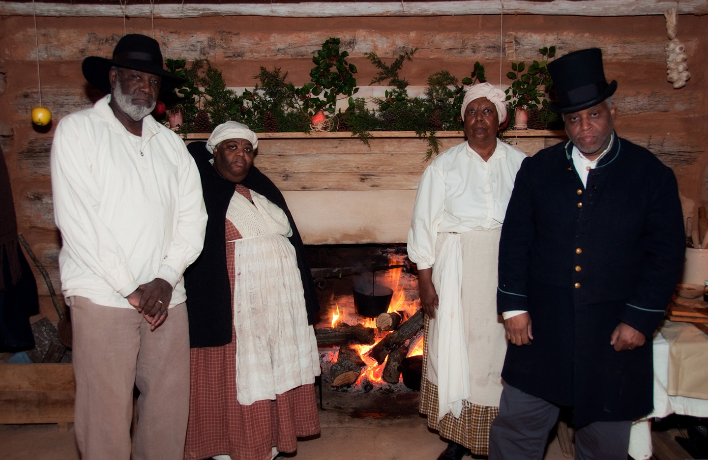 Four people dressed as enslaved people in front of the fireplace in cabin