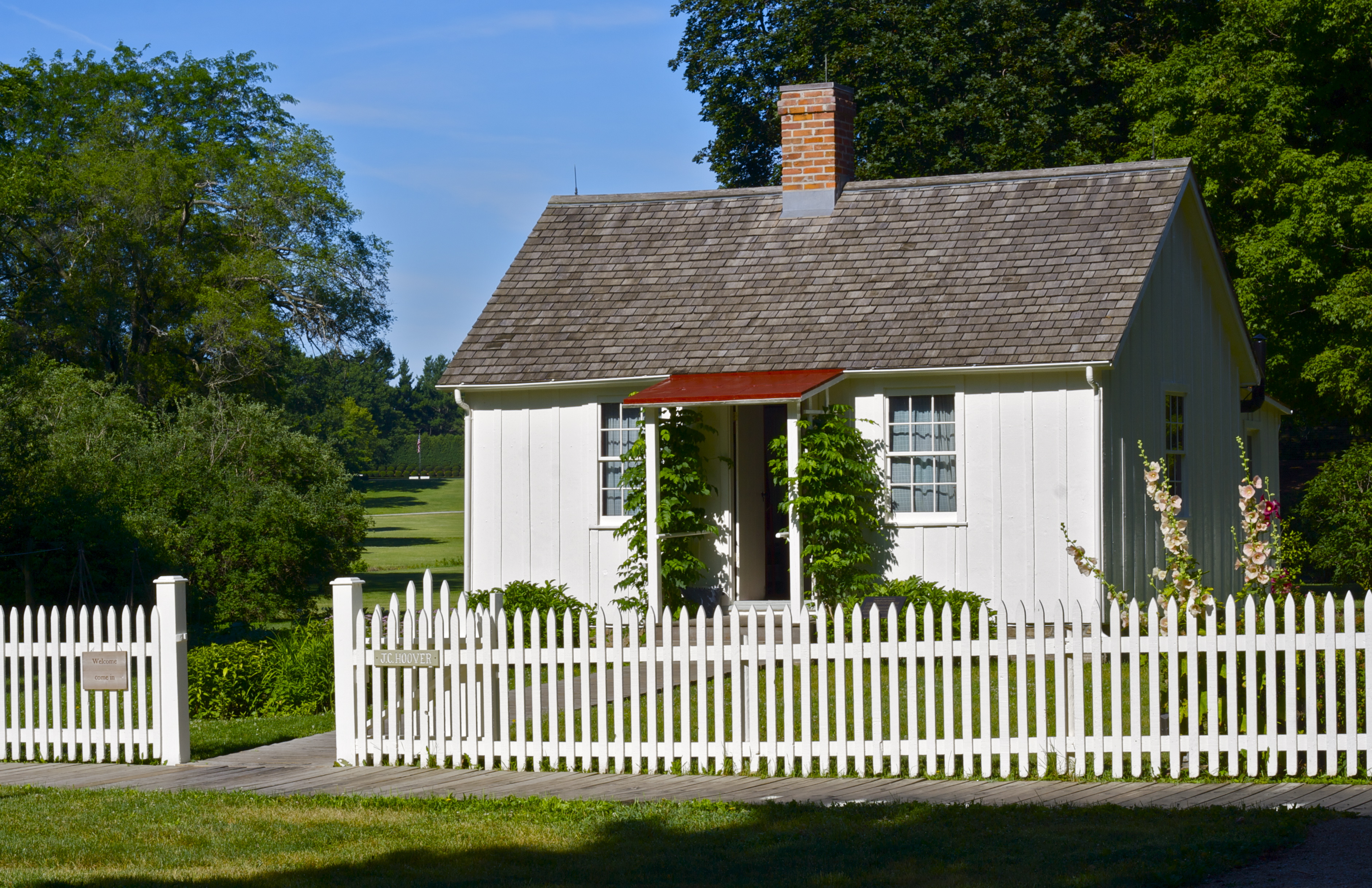 A one story wood frame house has board-and-batten exterior siding and a picket fence painted white.