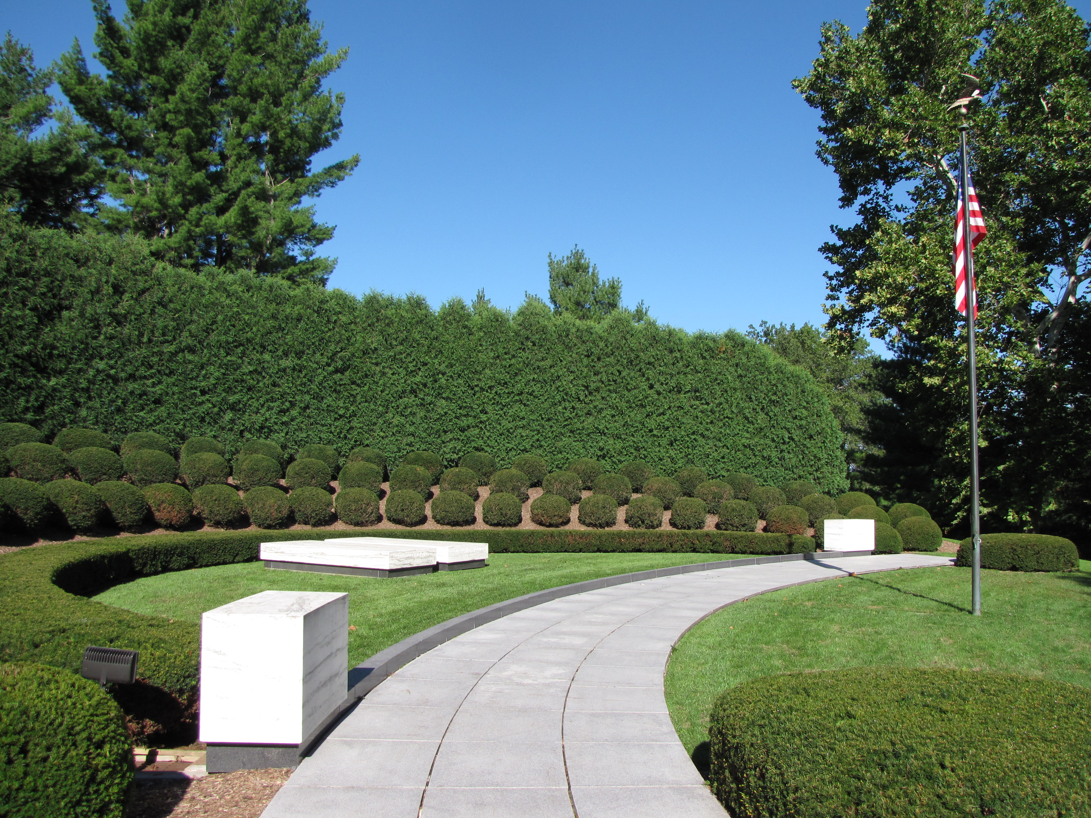 Two marble ledger stones each mark a grave in a semicircular landscaped plot with a flagpole.