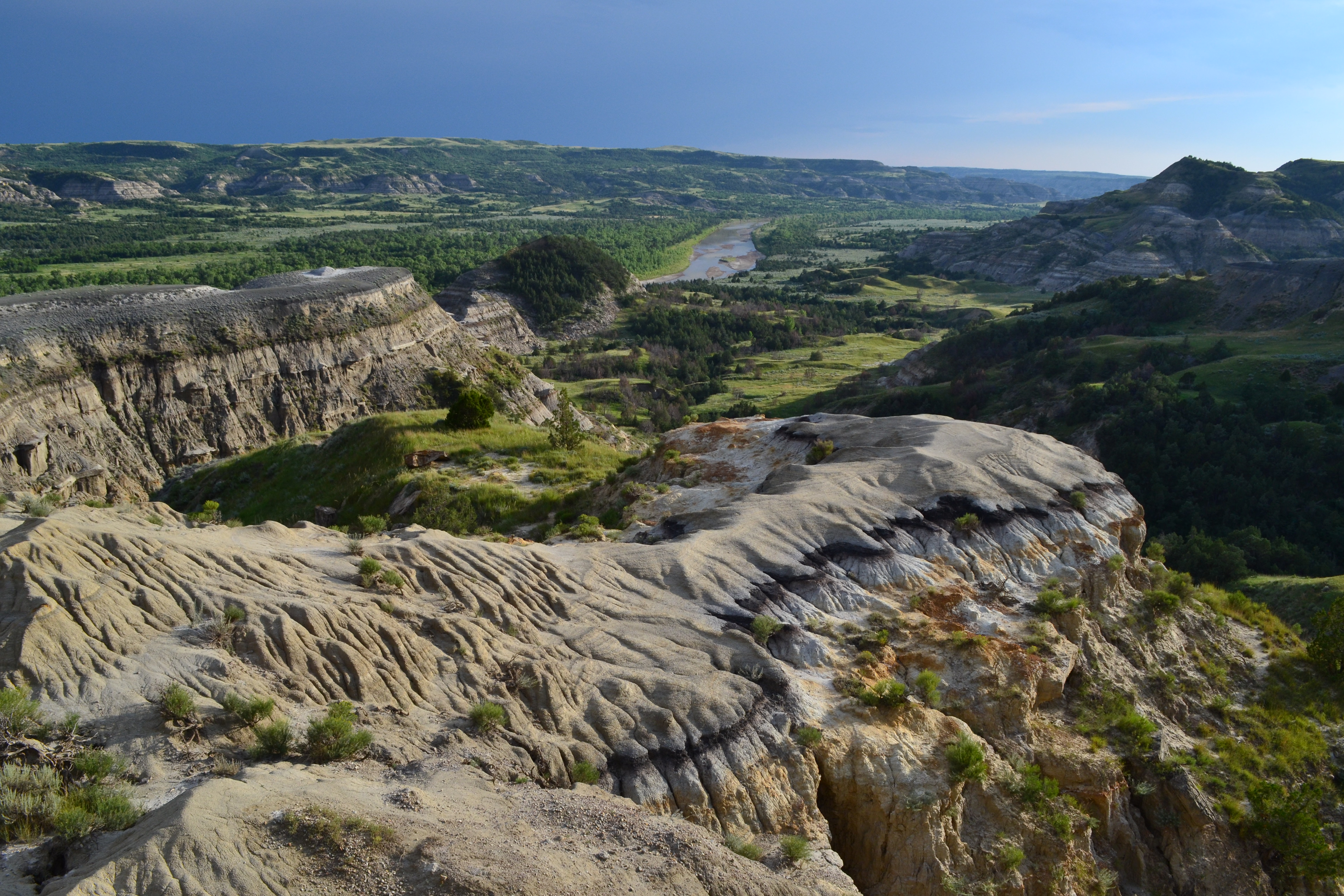 A colorfully striped butte in the foreground overlooks a dark green badlands landscape