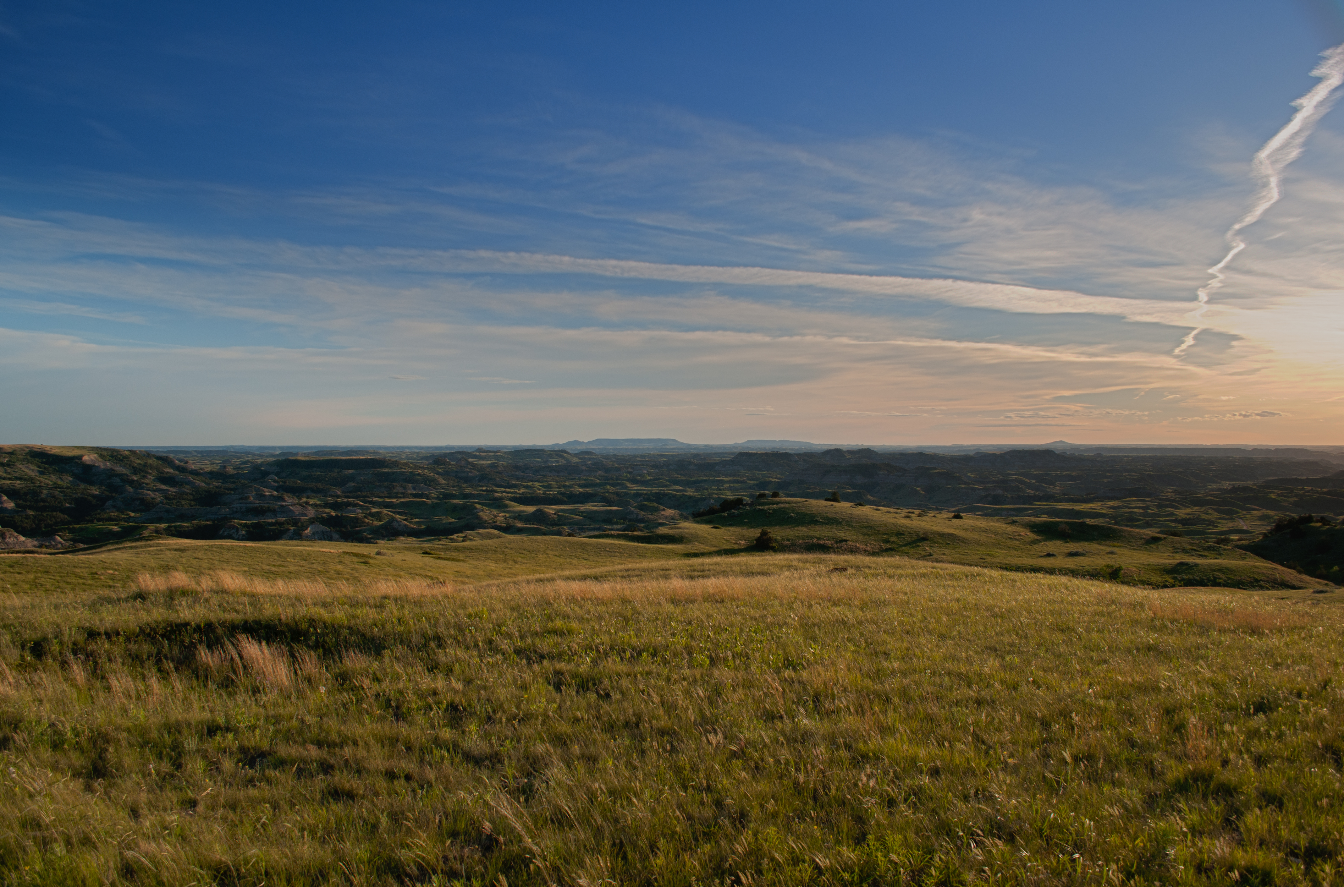 a green prairie hilltop overlooks the badlands, shrouded in shadows