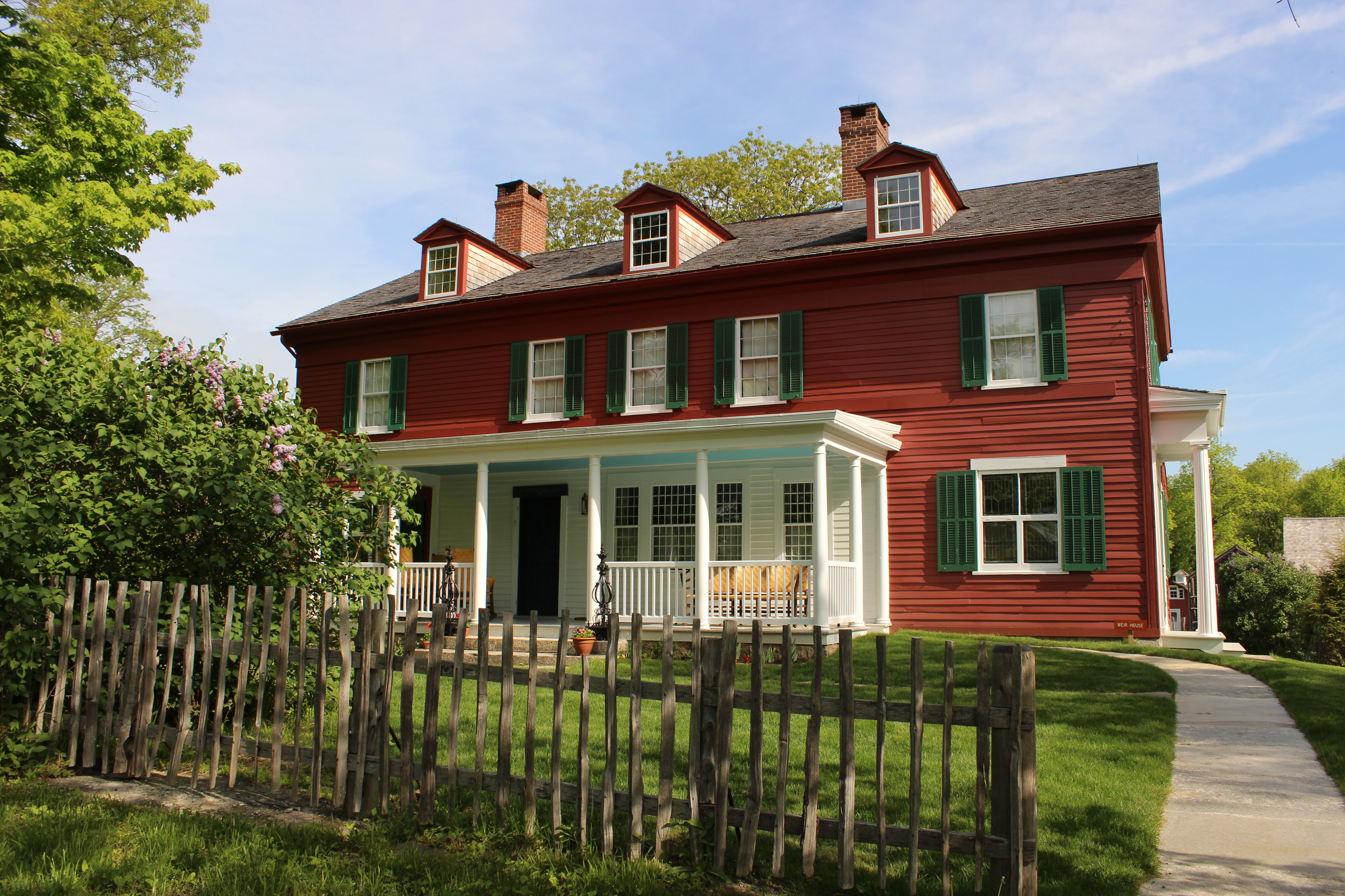 A view of the south side of the Weir House with porch visable, showing a fence in front of the home