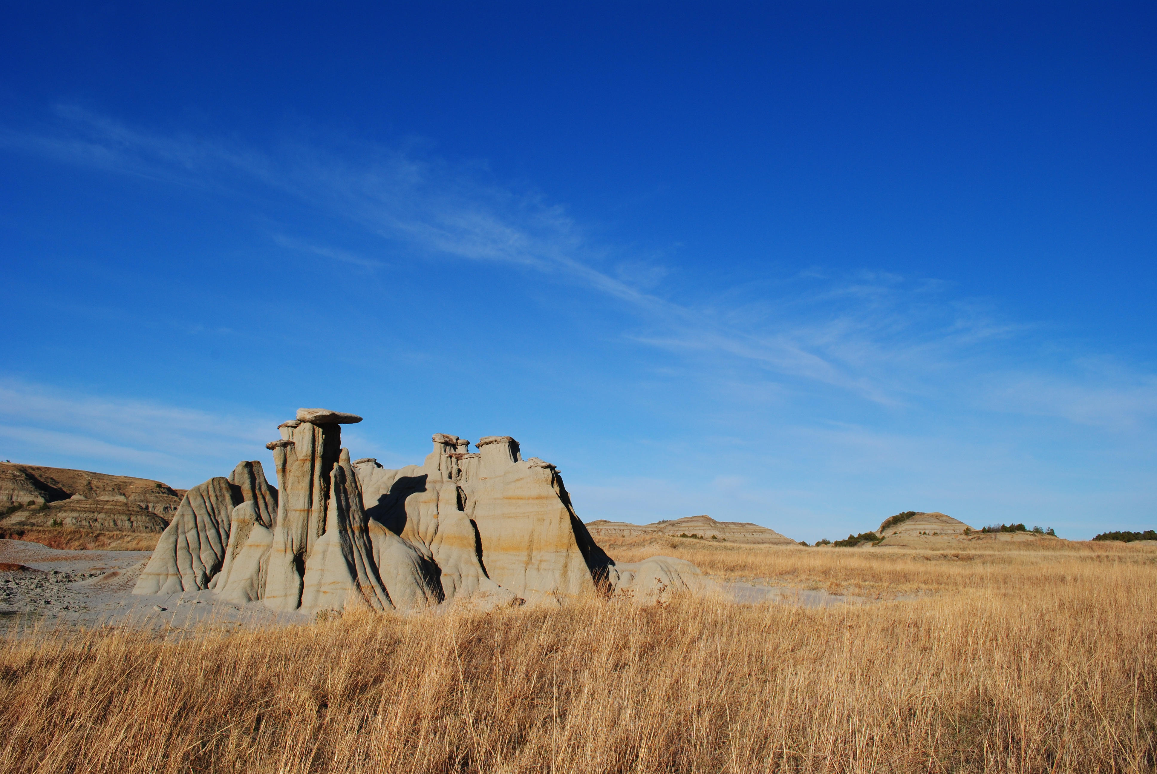 a strange looking sand and rock formation stands in a prairie of brown grass