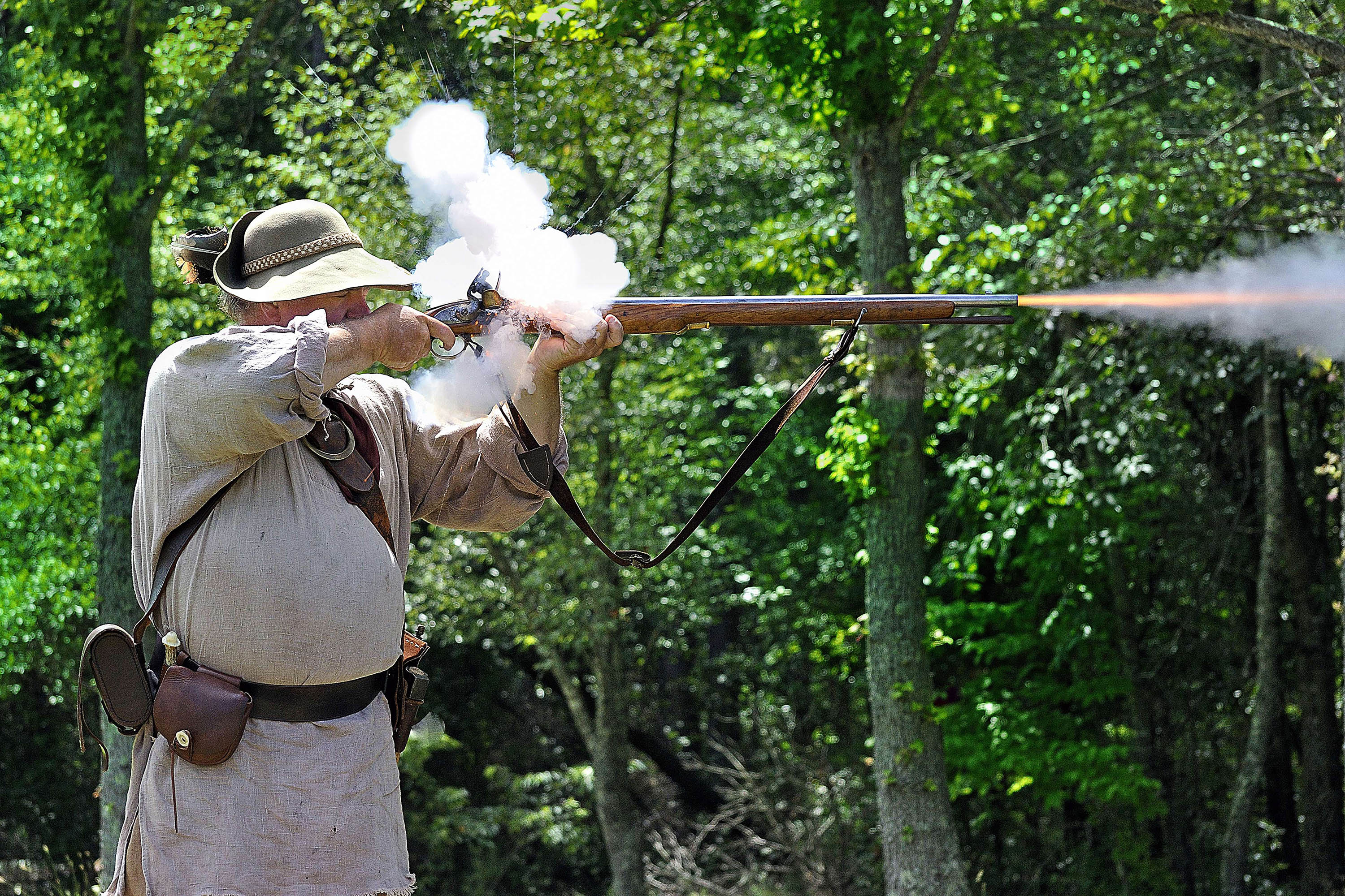 Smoke puffs up from the vent and a flame shoots out of the muzzle as a militiaman fires his musket.