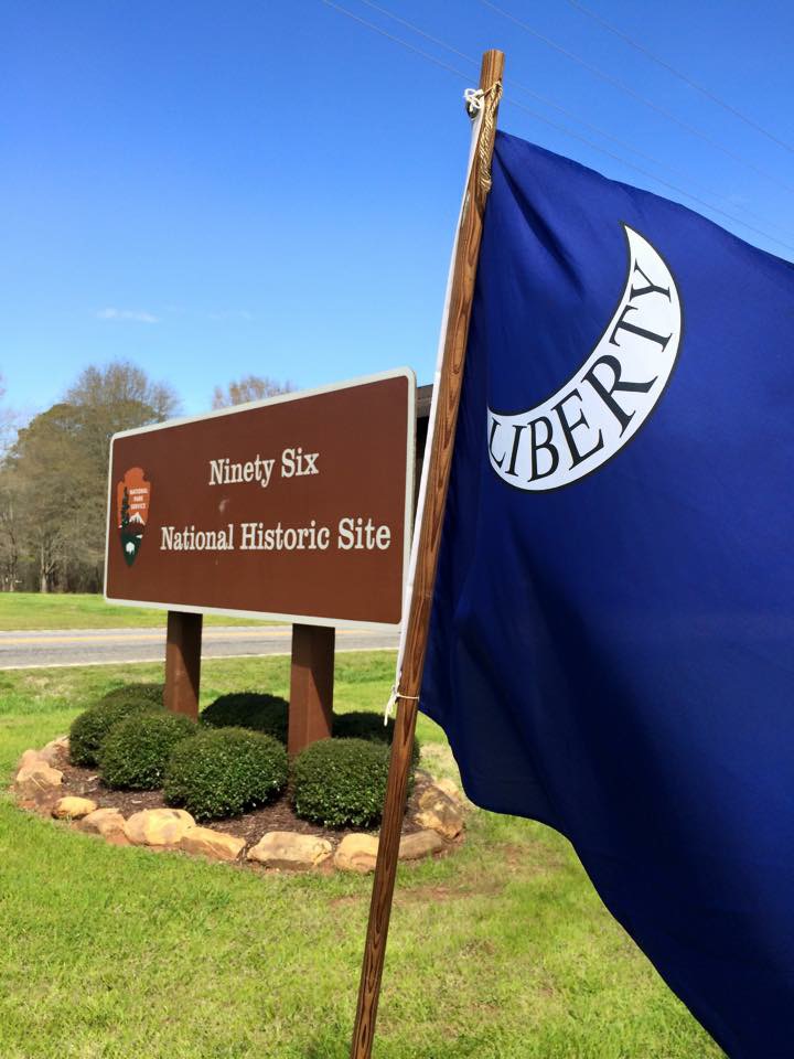 A blue Liberty flag is in the right foreground with the park entrance sign behind it.