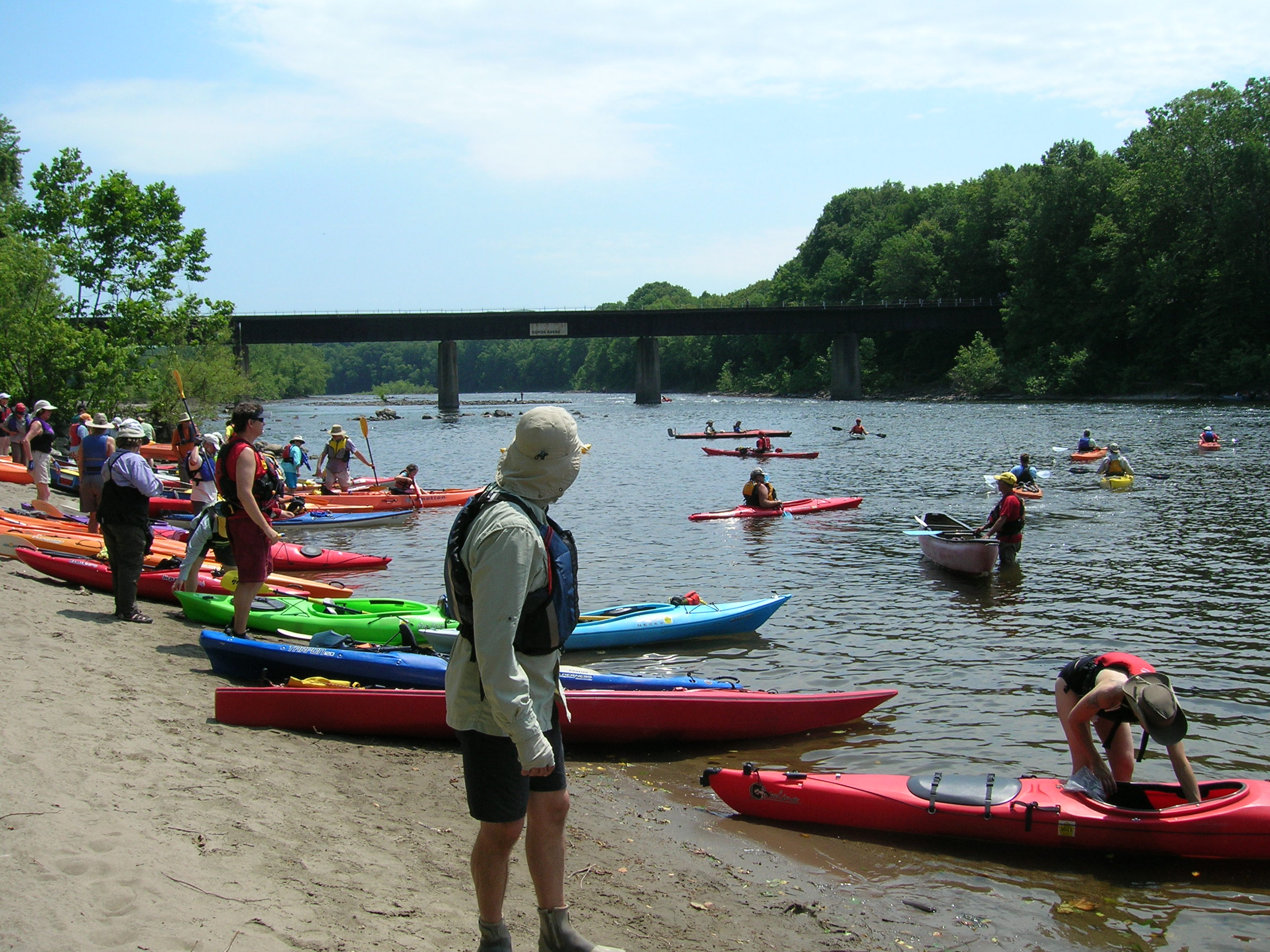 Kayakers enter the river from a riverside beach
