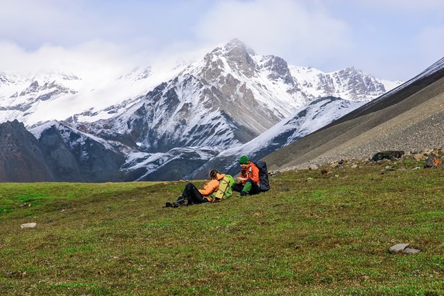 Two backpackers sitting in an alpine meadow with snowy mountains in the background