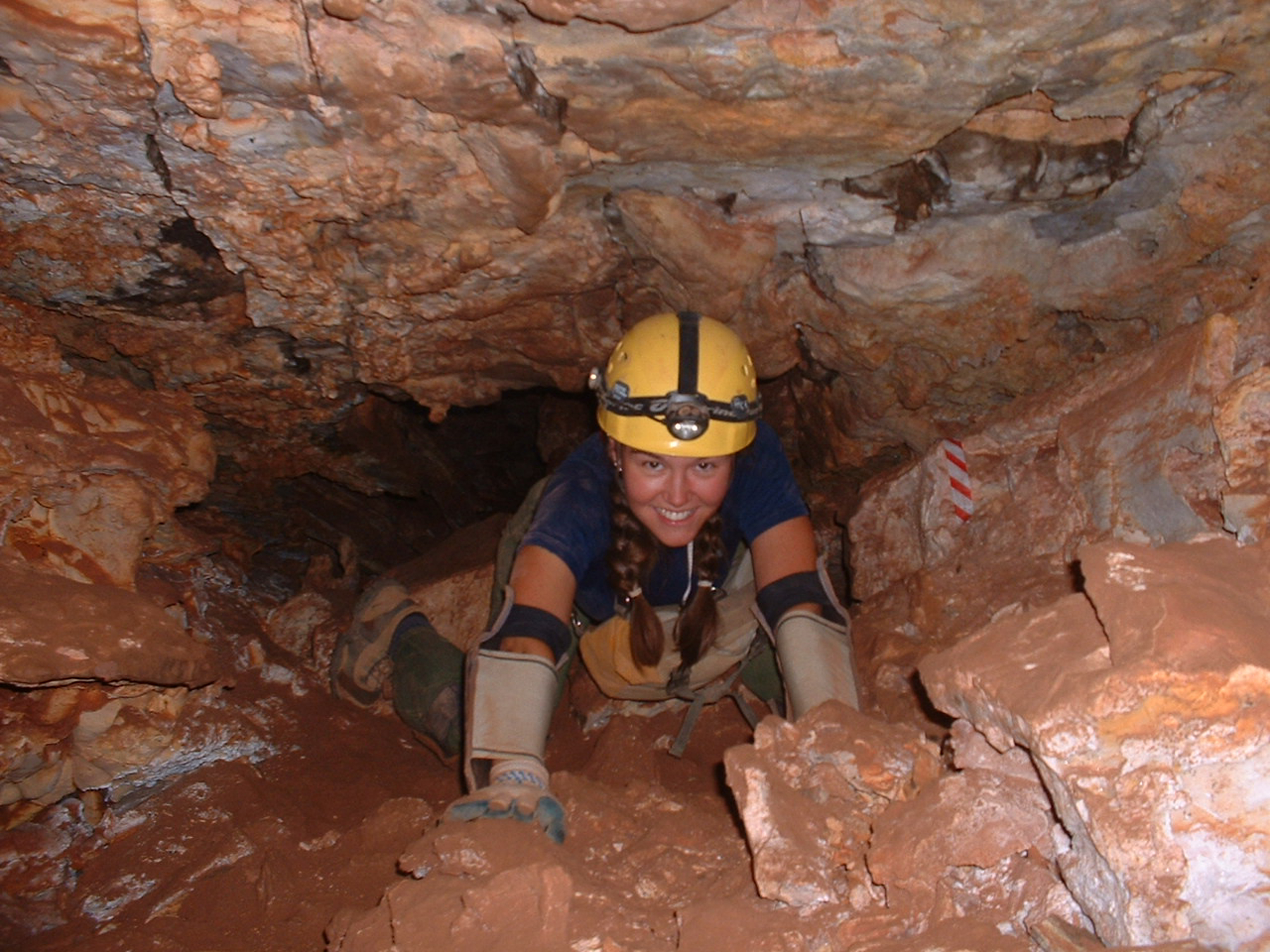 a caver with pads and helmet crawling in the cave