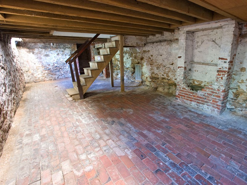Basement Color photo of the basement with brick floor, false chimney, and wooden staircase.