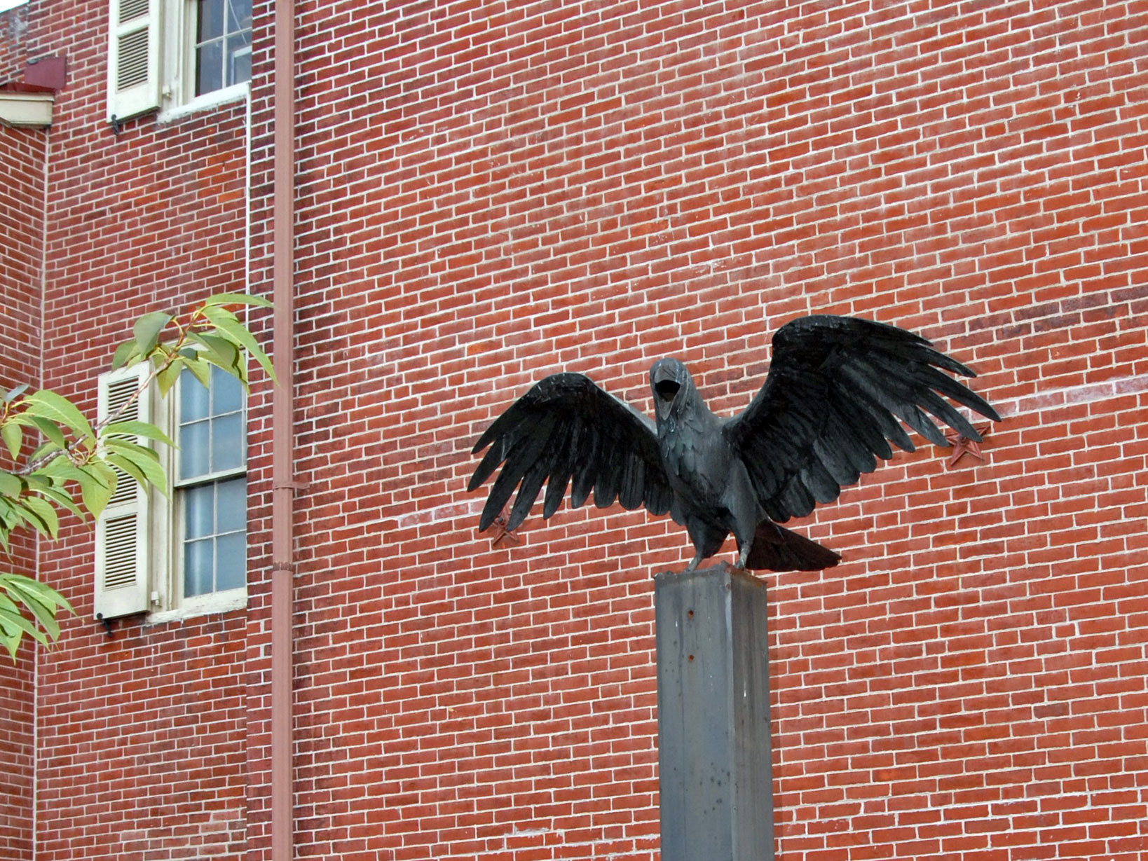 Color photo showing a large raven statue with wings outspread on a metal plinth.
