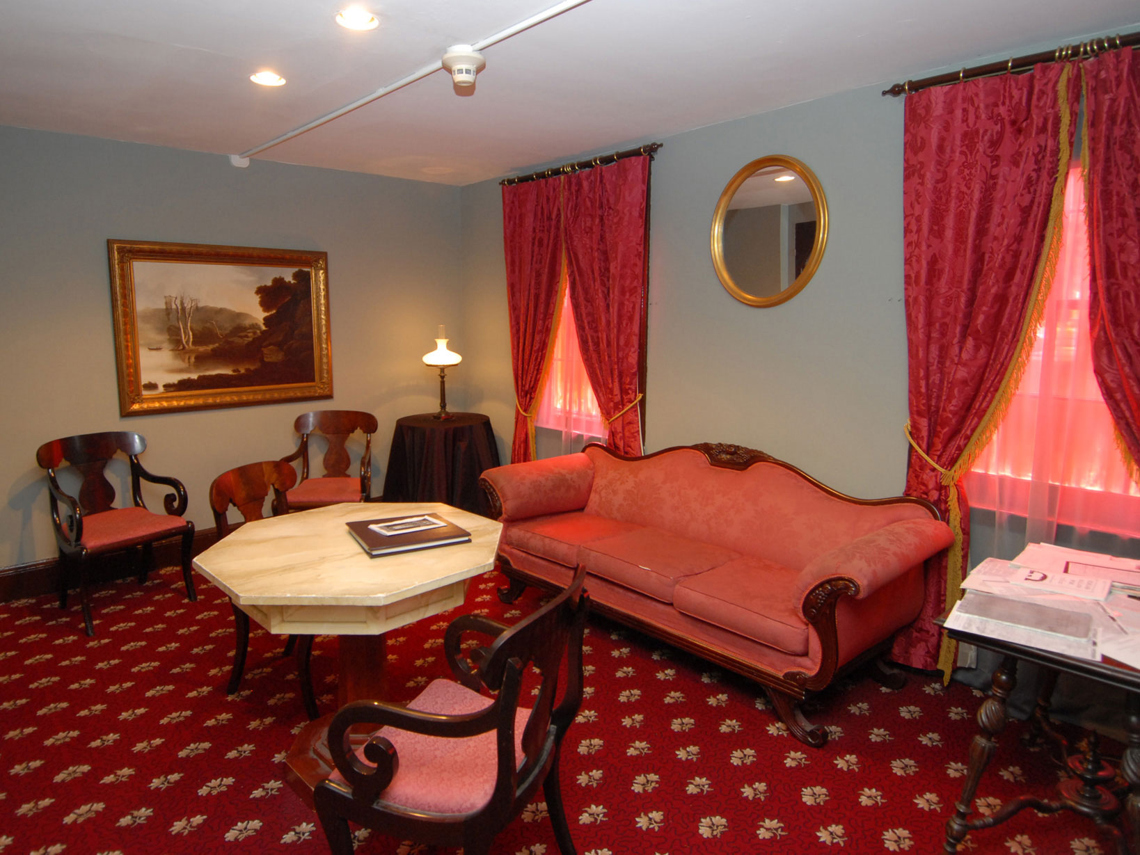 A small red-carpeted room with faux marble table, red upholstered chairs and sofa, and red curtains.