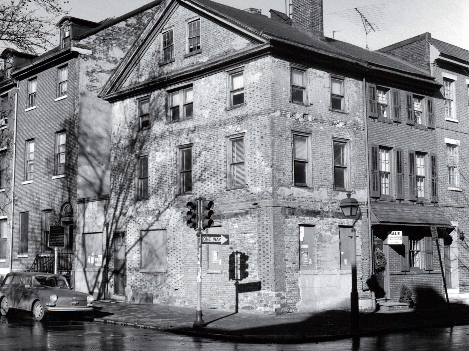 Black and white photo, circa 1960, showing a three story brick rowhouse situated on a corner lot.