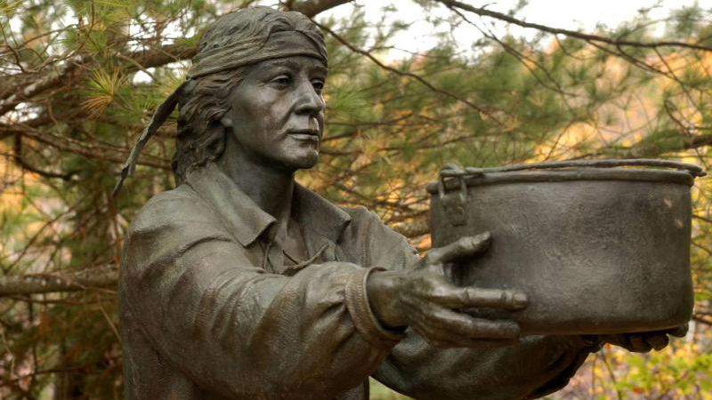 A bronze sculpture of a Passamaquoddy person reaching out to assist the French settlers.