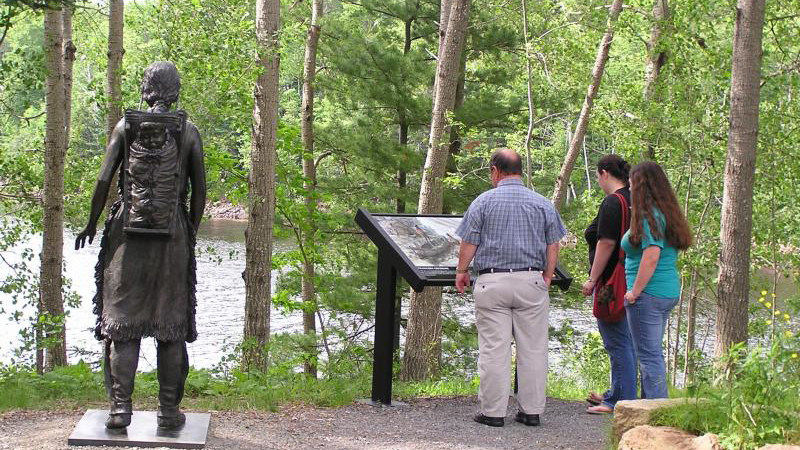 Three visitors read an interpretive wayside along the trail.