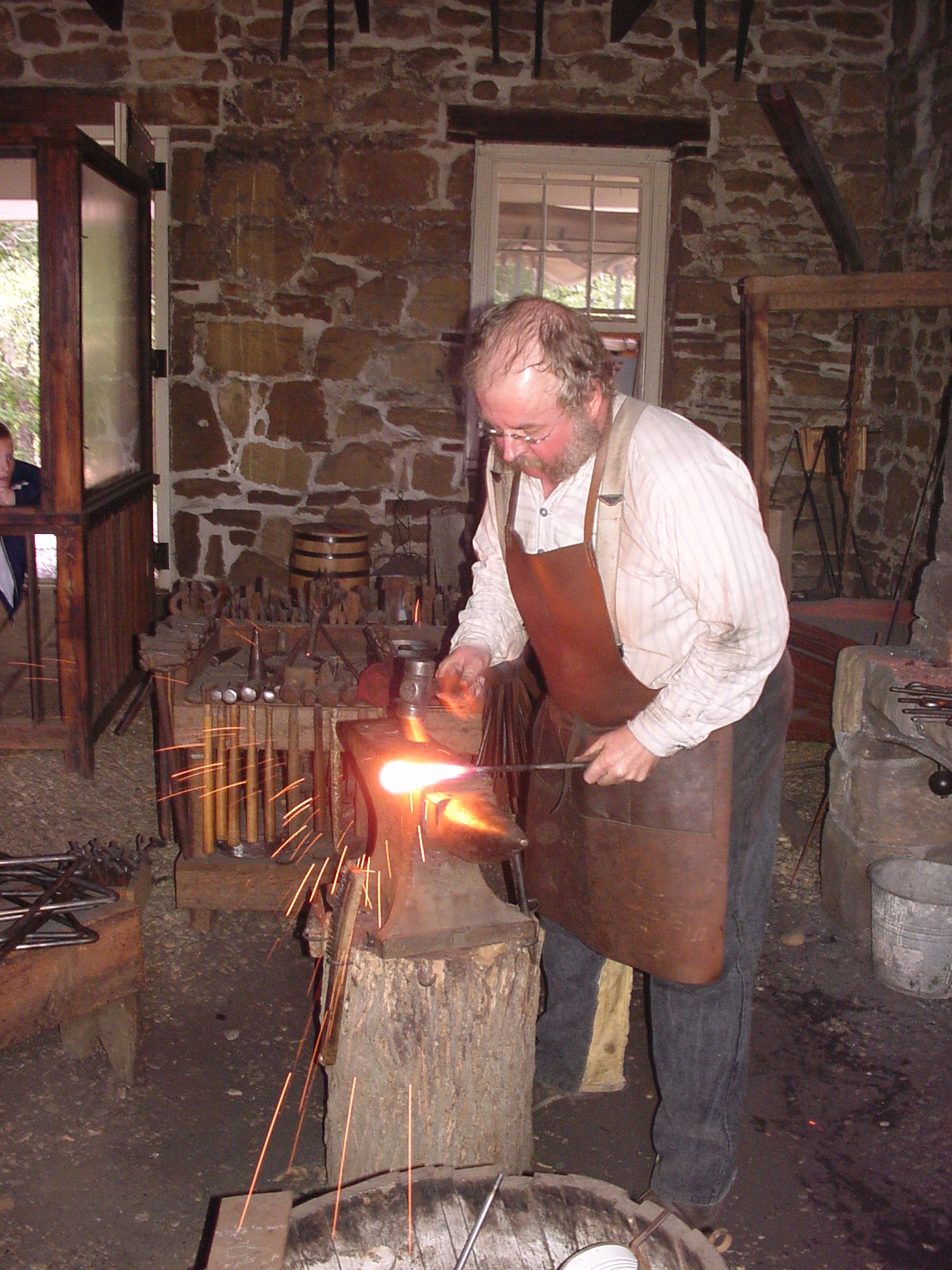 Man in leather apron hammering hot steel in blacksmith shop.