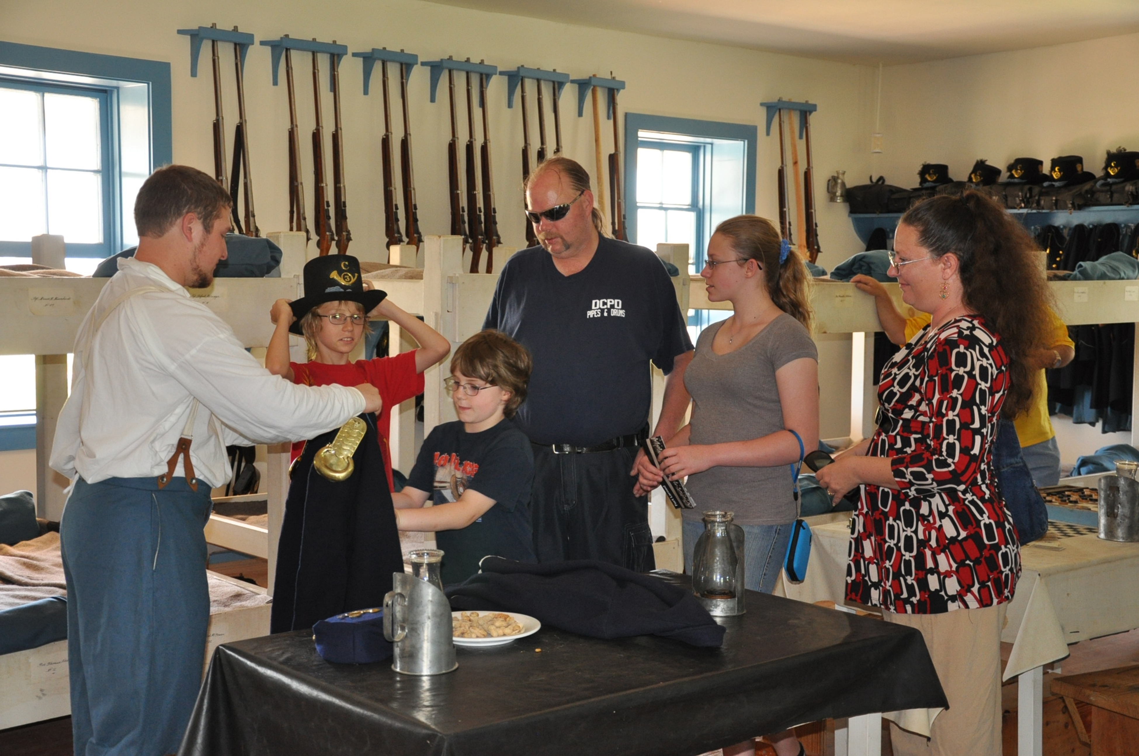 Man in 19th century U.S. Army uniform interacts with visitors in period barracks.