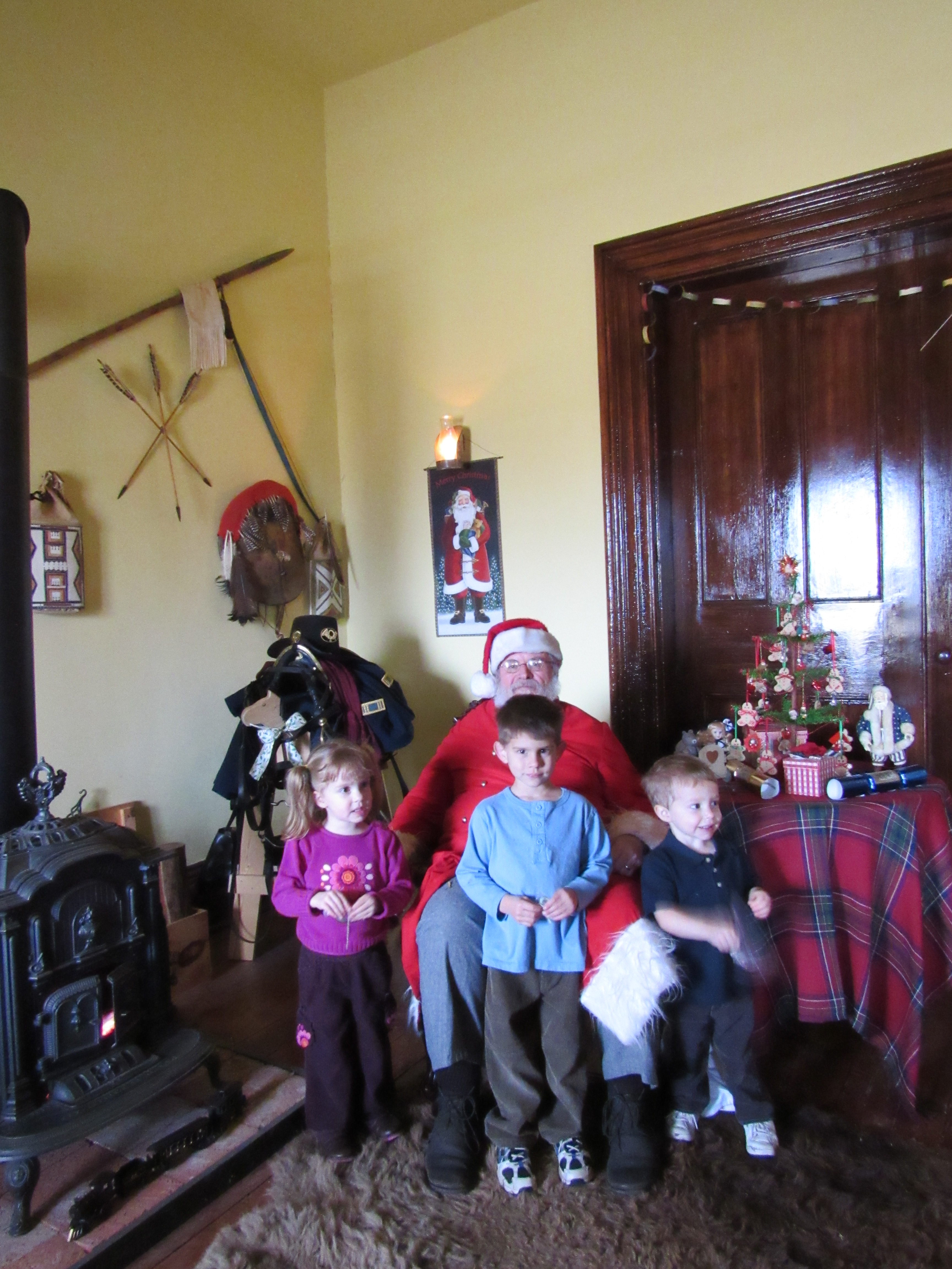 Three young children having their picture taken with Santa Claus in a period room.