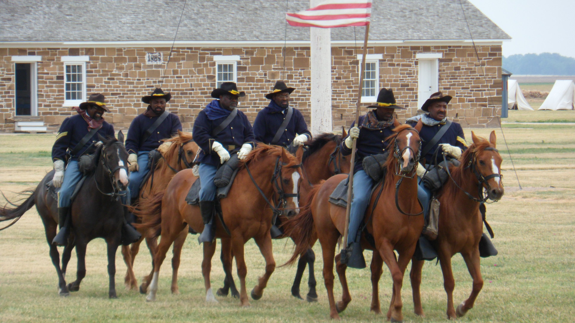 African American men in 19th century cavalry uniforms on horseback.
