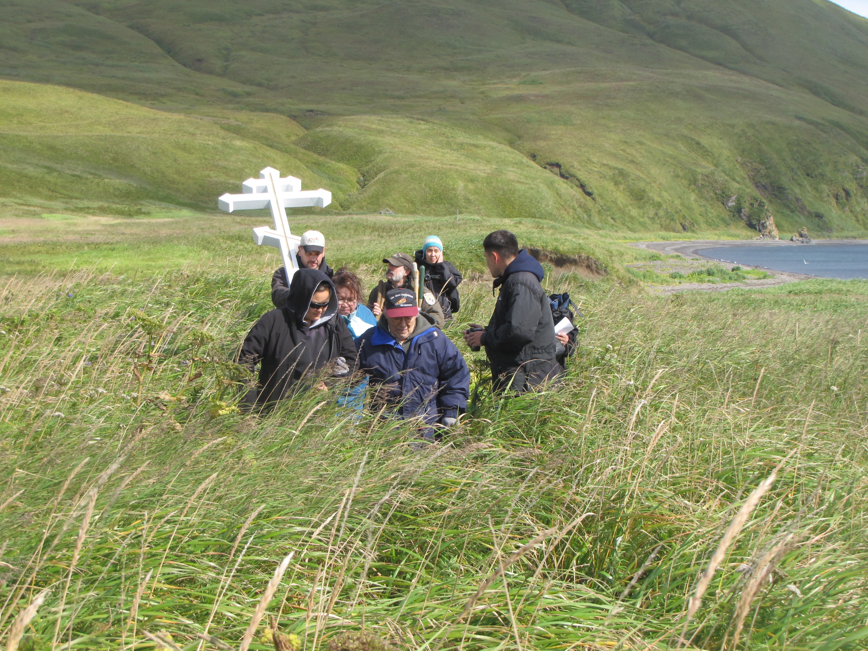 Group of people around a Russian cross in tall grass