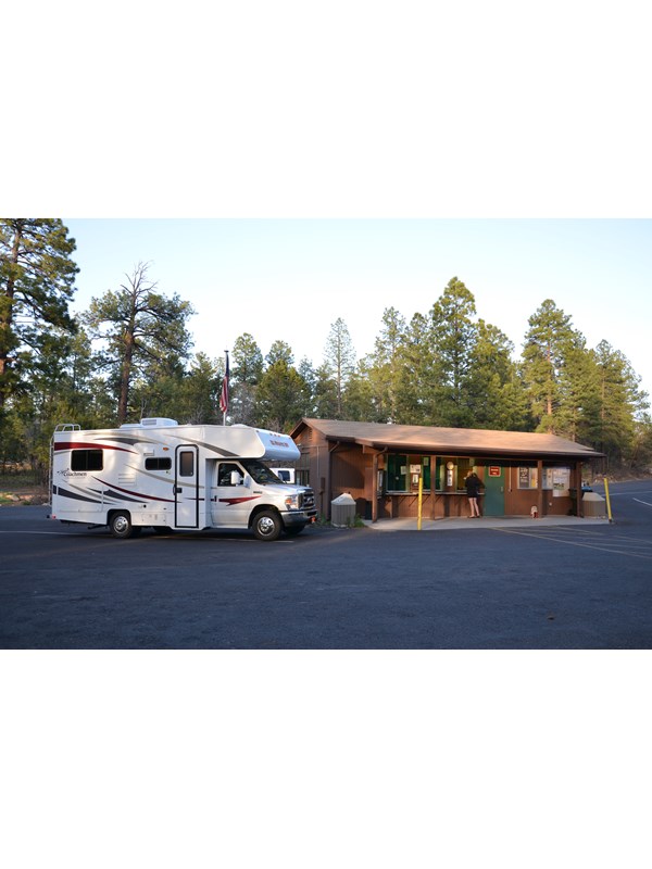 An RV is parked while people stand in in front of a small brown building