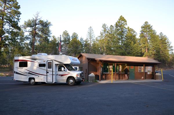 An RV is parked while people stand in in front of a small brown building