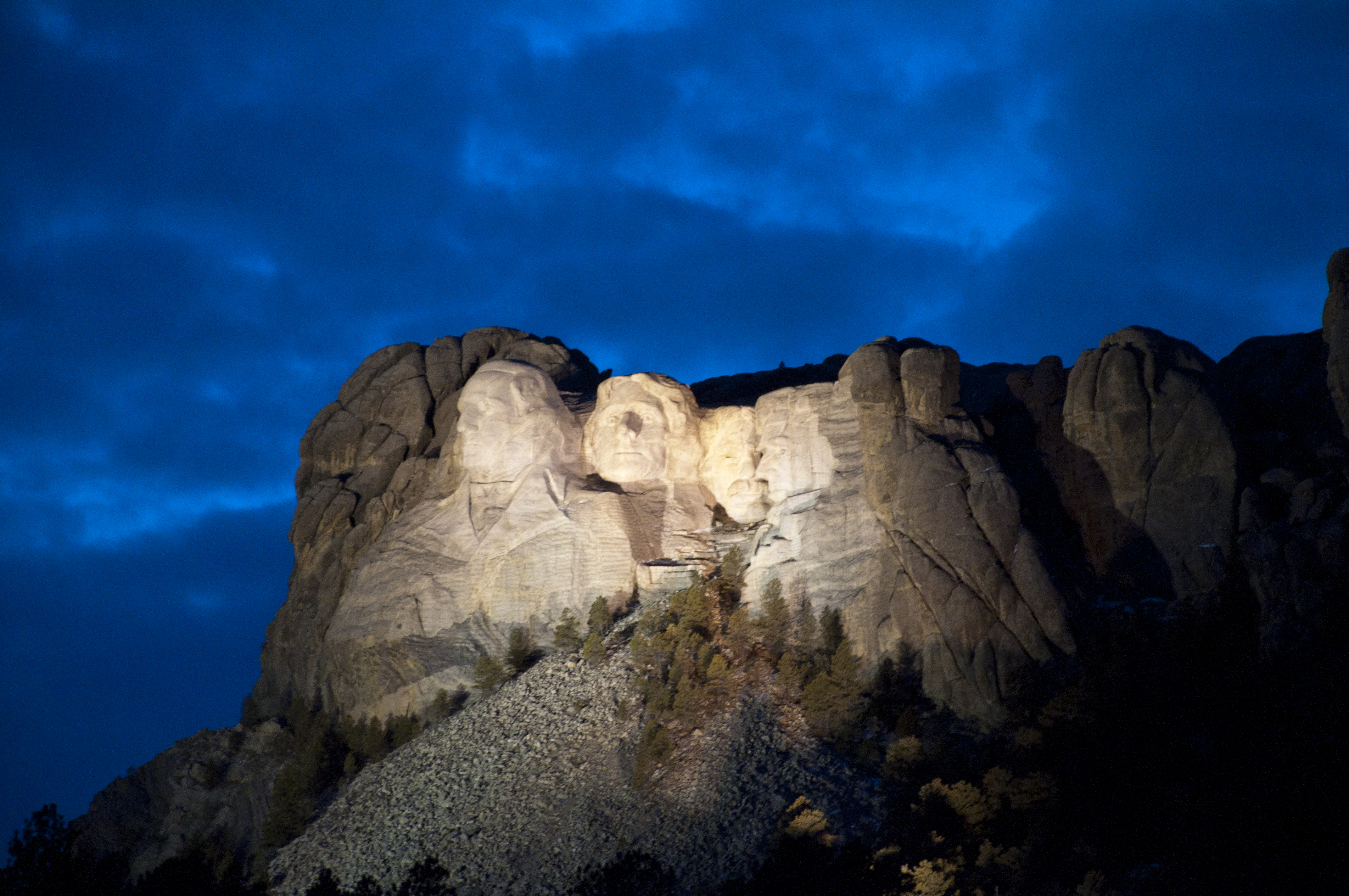 Mount Rushmore illuminated under a darkening evening sky.