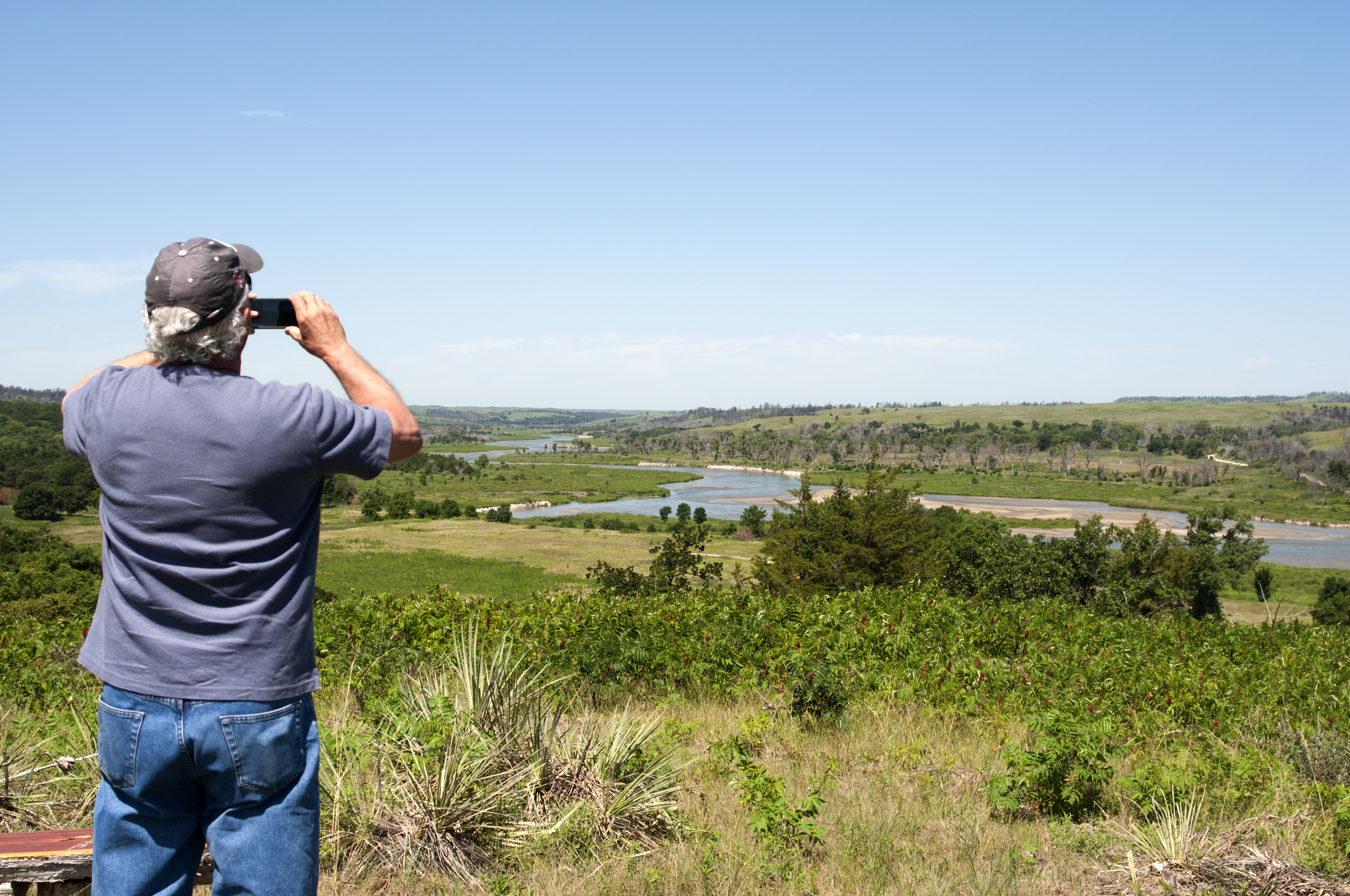 A man takes a photo of a meandering river from an overlook.