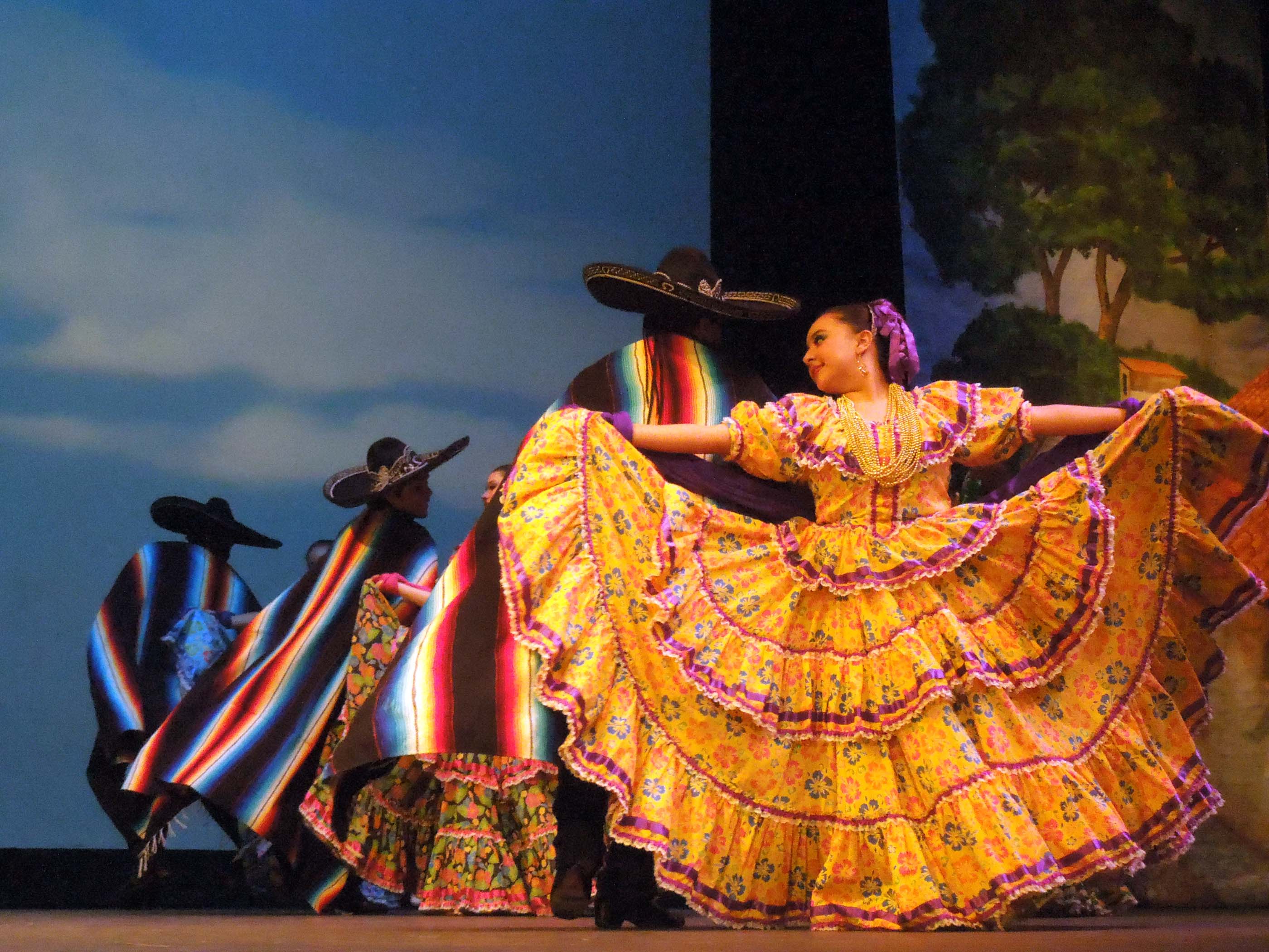 Women in swirling skirts and men with sombreros and colorful ponchos dance onstage