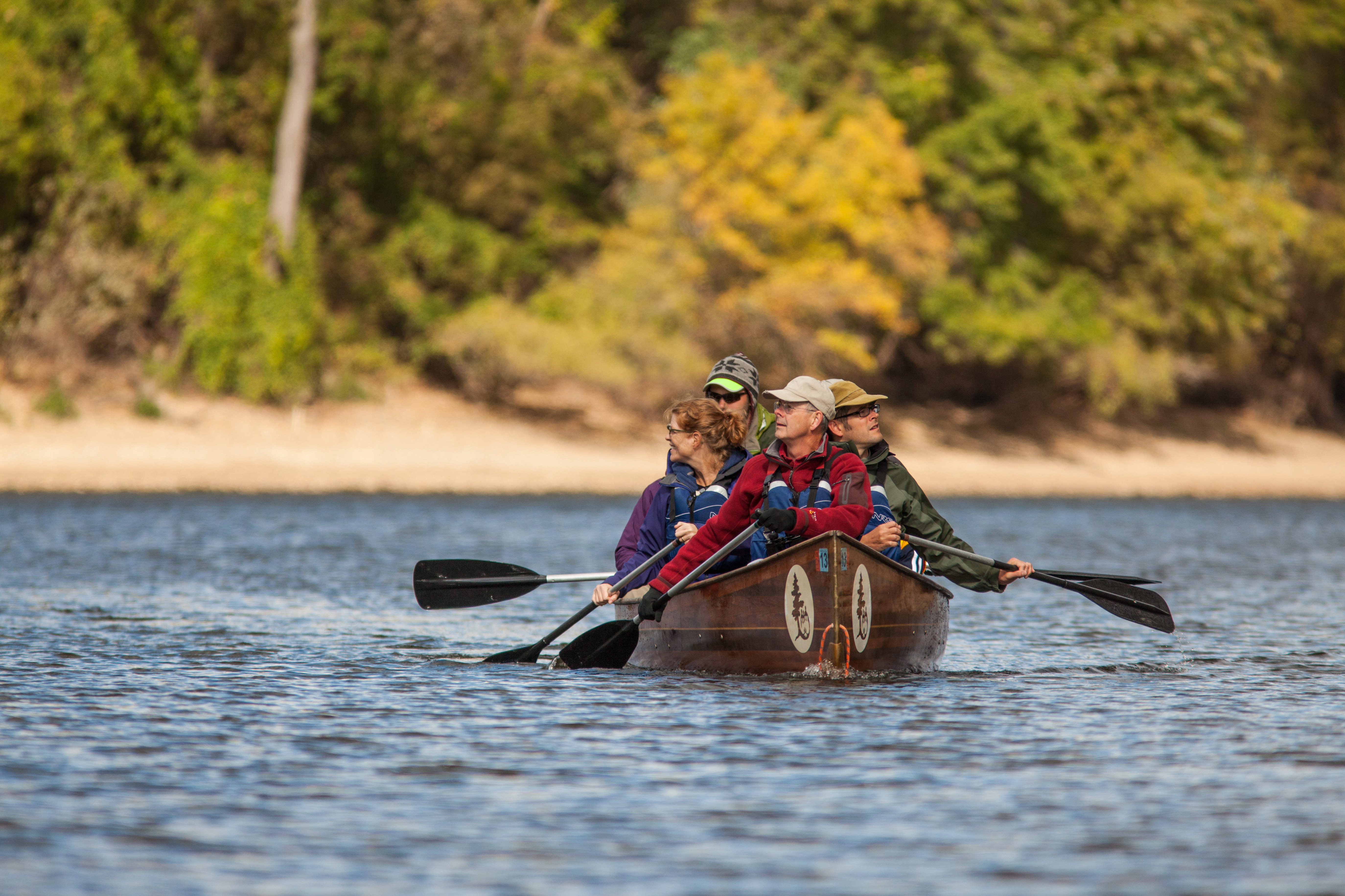 A large canoe filled with paddlers on the river surrounded by autumnal color.