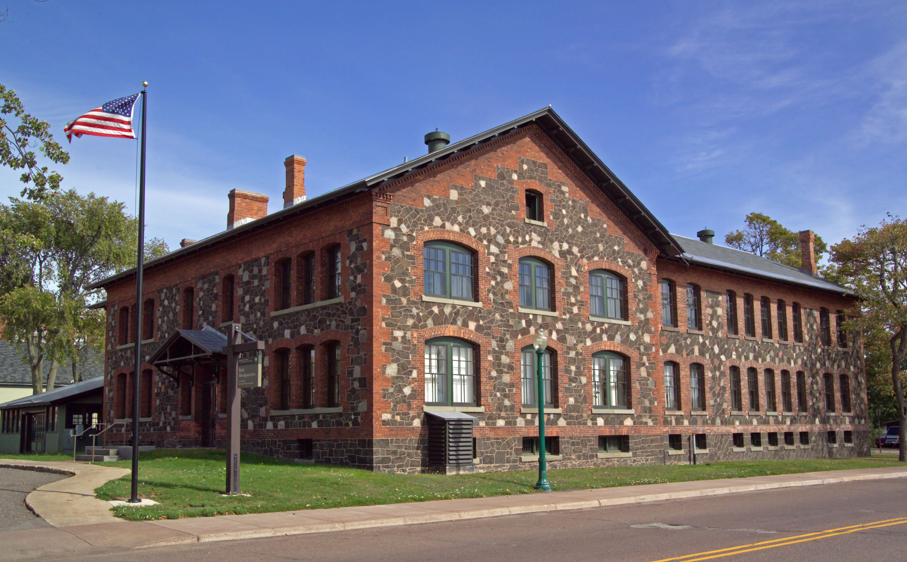 Two story stone and brick building. The American flag flies in front of a blue sky background